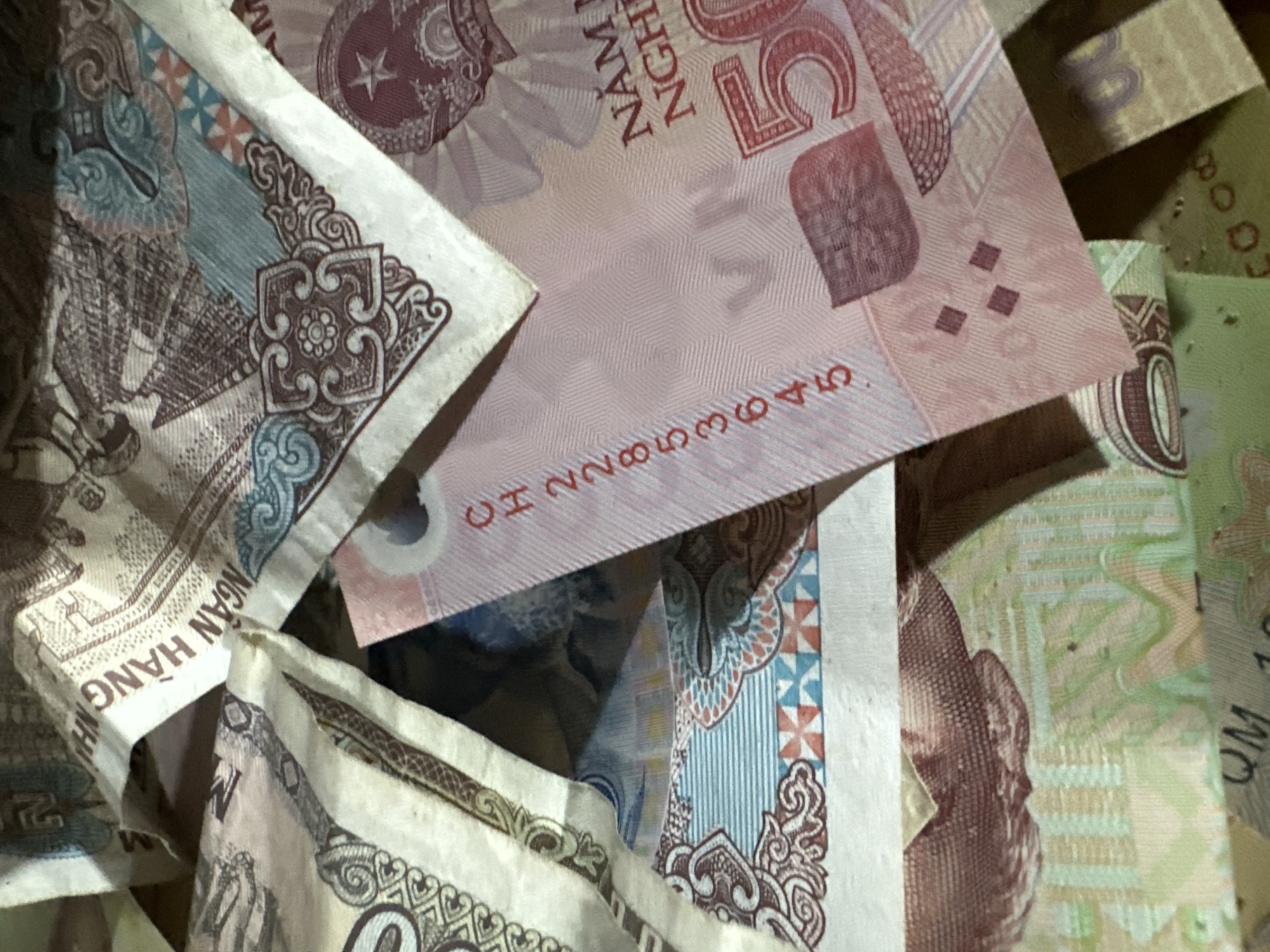 Close-up of Vietnamese Dong currency, specifically 50,000 VND notes, partially visible and piled together. The scene is likely located in Sà Phìn Commune, Vietnam.