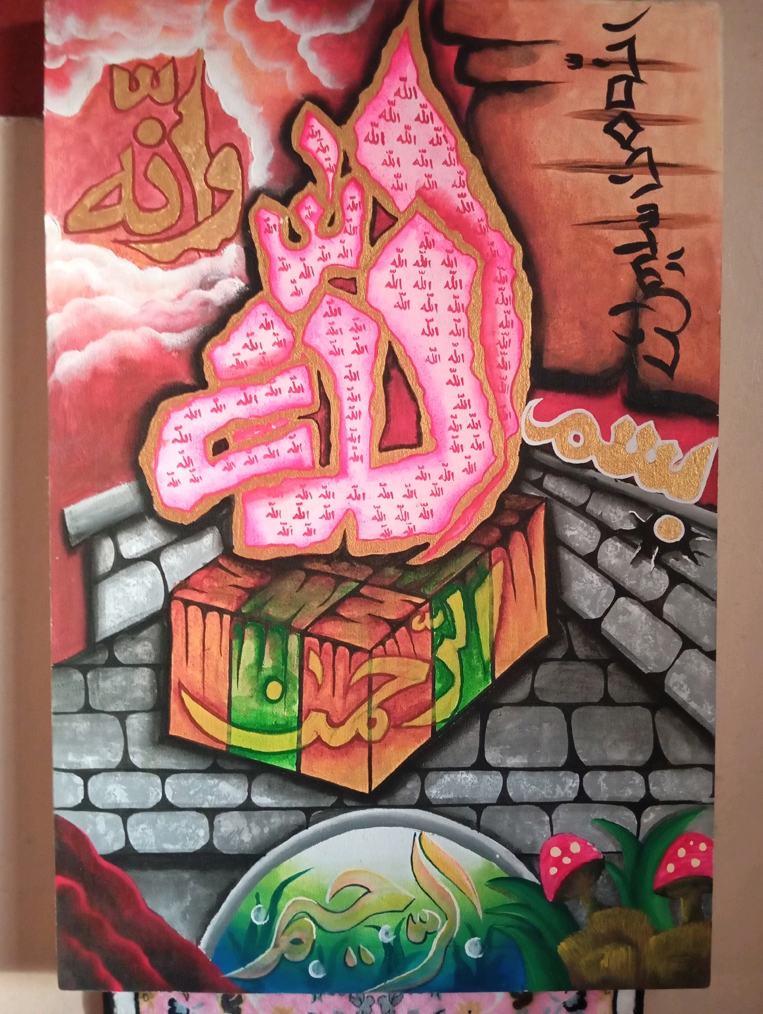 This is a painting, not a photograph. The painting features stylized Islamic calligraphy, predominantly in pink with gold accents, forming a large, abstract shape resembling a hand or a fiery entity. Within this form, smaller Arabic script, which appears to be the word "Allah" repeated, is visible. To the left, gold Arabic calligraphy is set against a backdrop of pink clouds. The central calligraphic element rests on a rectangular block painted with vibrant colors like orange, green, and yellow, with abstract designs. This block sits on a surface resembling a stone wall made of grey bricks. To the right, black Arabic calligraphy is rendered vertically on a brown textured background. Below the stone wall, there's a circular area with green and blue hues, containing more abstract calligraphy and what appear to be stylized bubbles. The bottom right corner of the painting depicts two red and white spotted mushrooms and green foliage. The painting is framed by a light brown border. There are no people or discernible city elements like buildings or landmarks of Jarit, Indonesia present in the artwork.