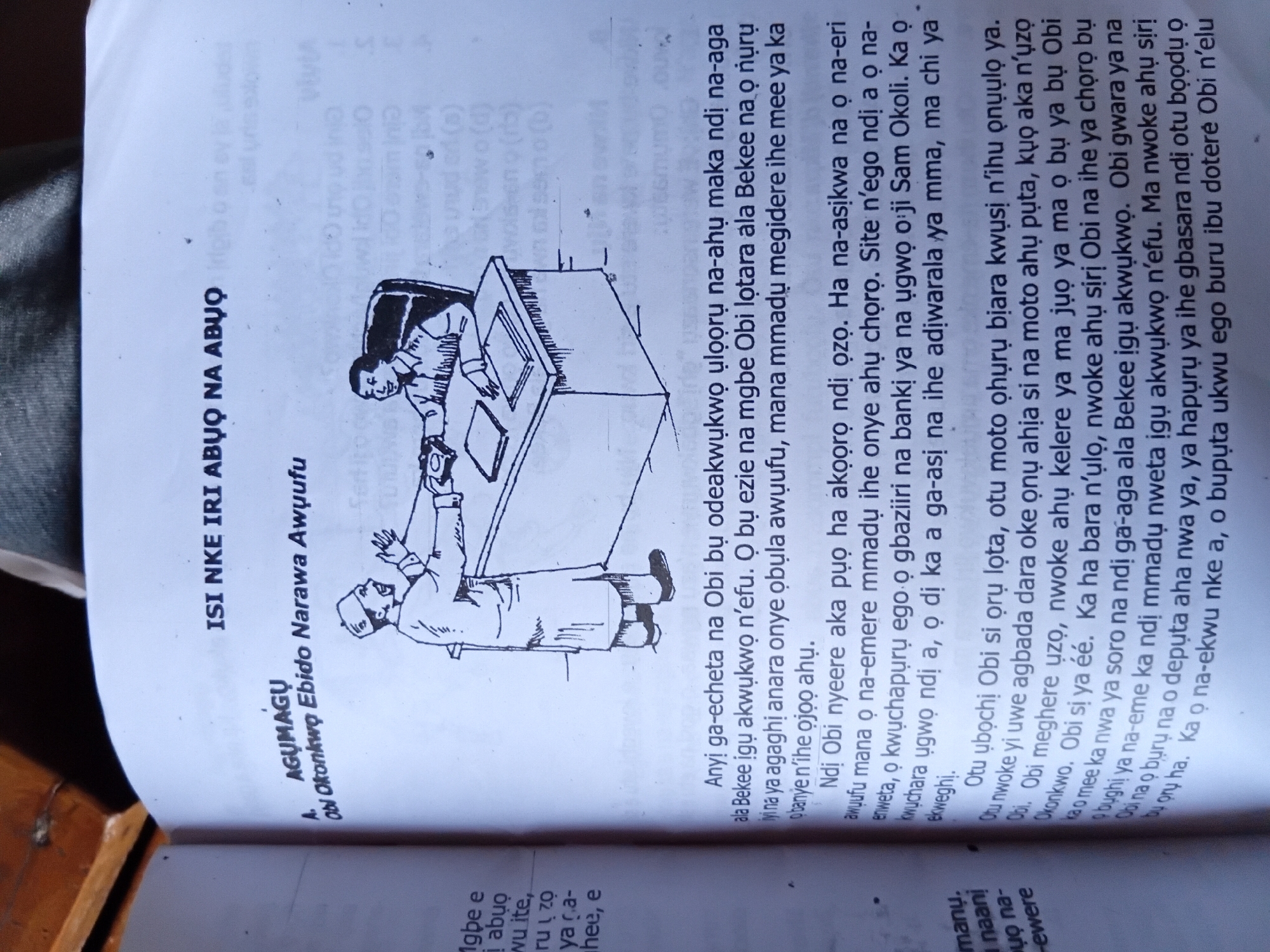 The image shows a page from a book with text and an illustration. The illustration depicts two men in a meeting. One man, wearing a hat and traditional attire, stands while gesturing towards the other man, who is seated behind a desk. The seated man is wearing a collared shirt and appears to be listening. The desk has papers and what looks like a telephone on it.
The text is in the Igbo language. The title at the top reads "ISI NKE IRI ABUO NA ABUO". Below this, there is a section labeled "A. AGUMAGU" and a subtitle "Obi Okonkwo Ebido Narawa Awuufu". The main body of text describes events and interactions, seemingly related to the characters mentioned.
While the text is in Igbo, a language spoken in Nigeria, the image does not provide any specific visual cues to definitively place the location within Nkpor, Nigeria. The scene is a generic depiction of a meeting or a discussion.