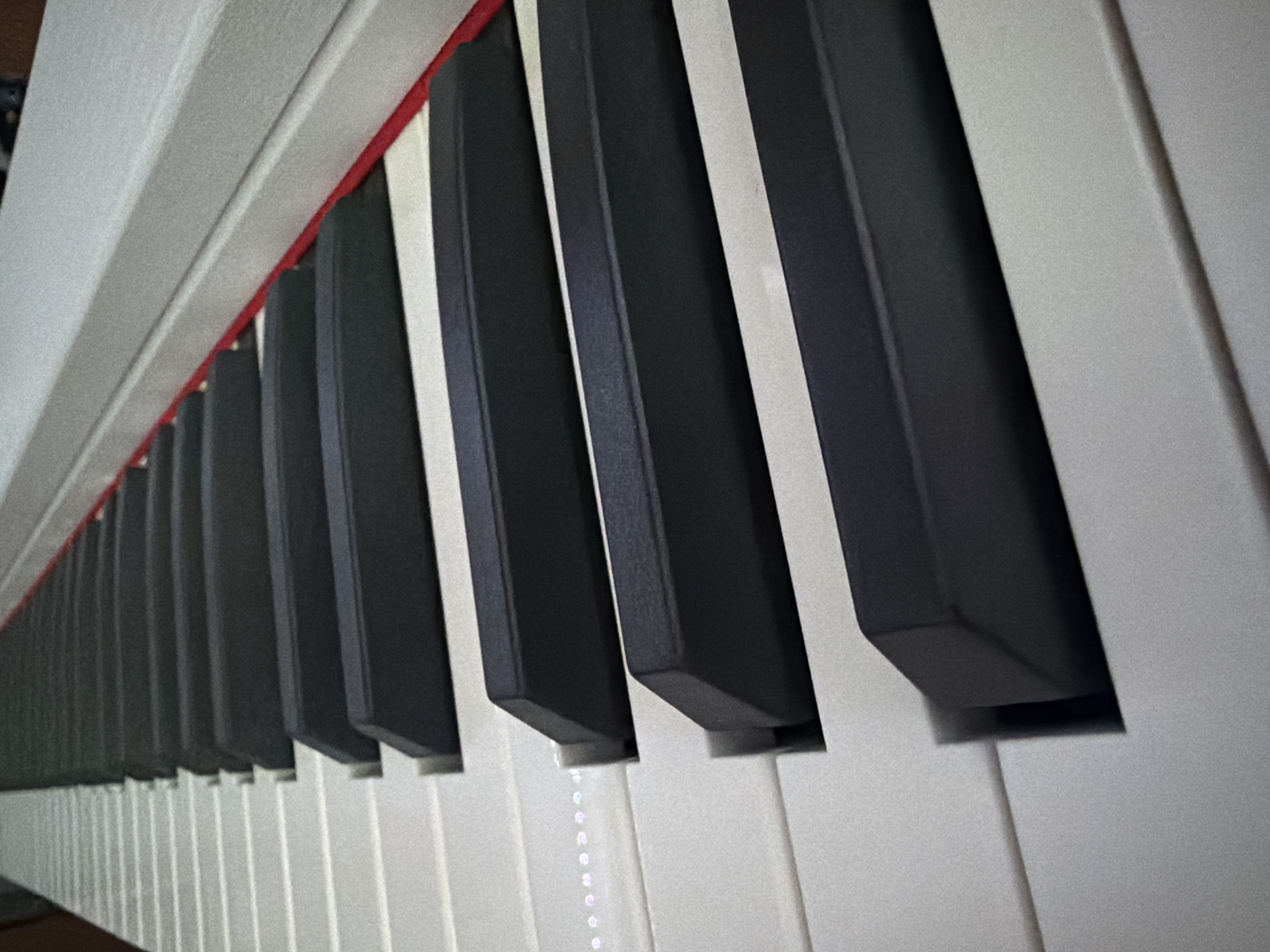 The image shows a close-up, angled view of a piano keyboard. The black and white keys are in focus, with the perspective compressing the rows of keys further into the background. A red strip is visible along the top edge of the keys. The lighting creates a slight sheen on the key surfaces. The image does not contain sufficient information to determine its location in Bugulma, Russia or provide any information regarding people, actions, interactions, or the environment.