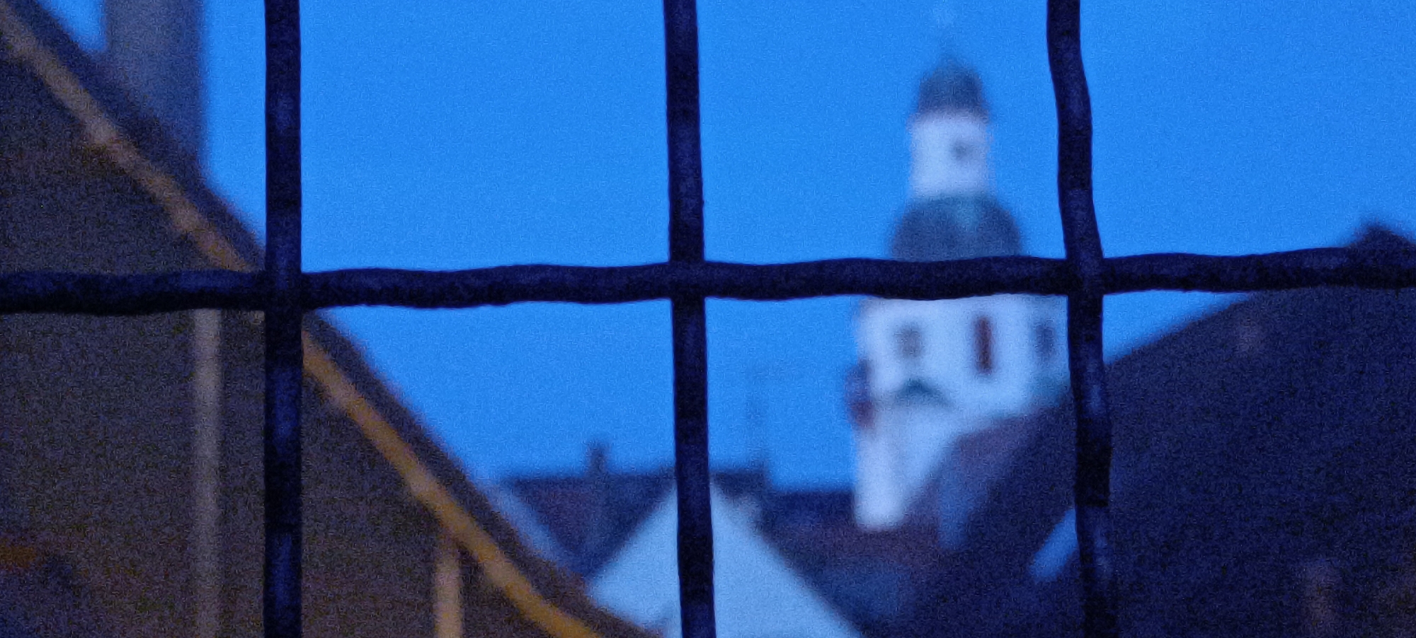 The image, taken at dusk or early morning, shows a view through a dark, lattice-like structure, possibly a fence or grate. In the background, a white building with a dark-domed tower, resembling a church or historic public building, is visible against a clear blue sky. The lower portion of the image reveals the dark outlines of adjacent buildings. The overall impression is a subdued urban scene. Based on available information, this view is likely from the vicinity of the historic town hall and church located in the market square of Winnenden, Germany.