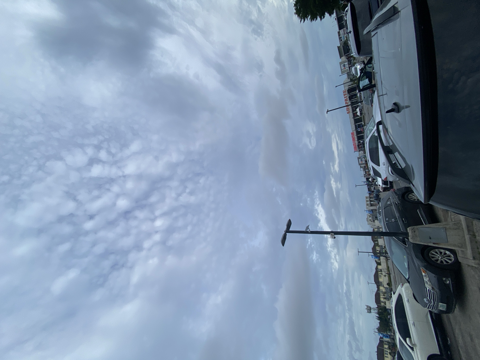The image shows a parking lot with cars parked along the edge, adjacent to a Shoprite supermarket, potentially in Sangotedo, Nigeria. Overcast skies dominate the view. Streetlights are visible alongside parked cars.