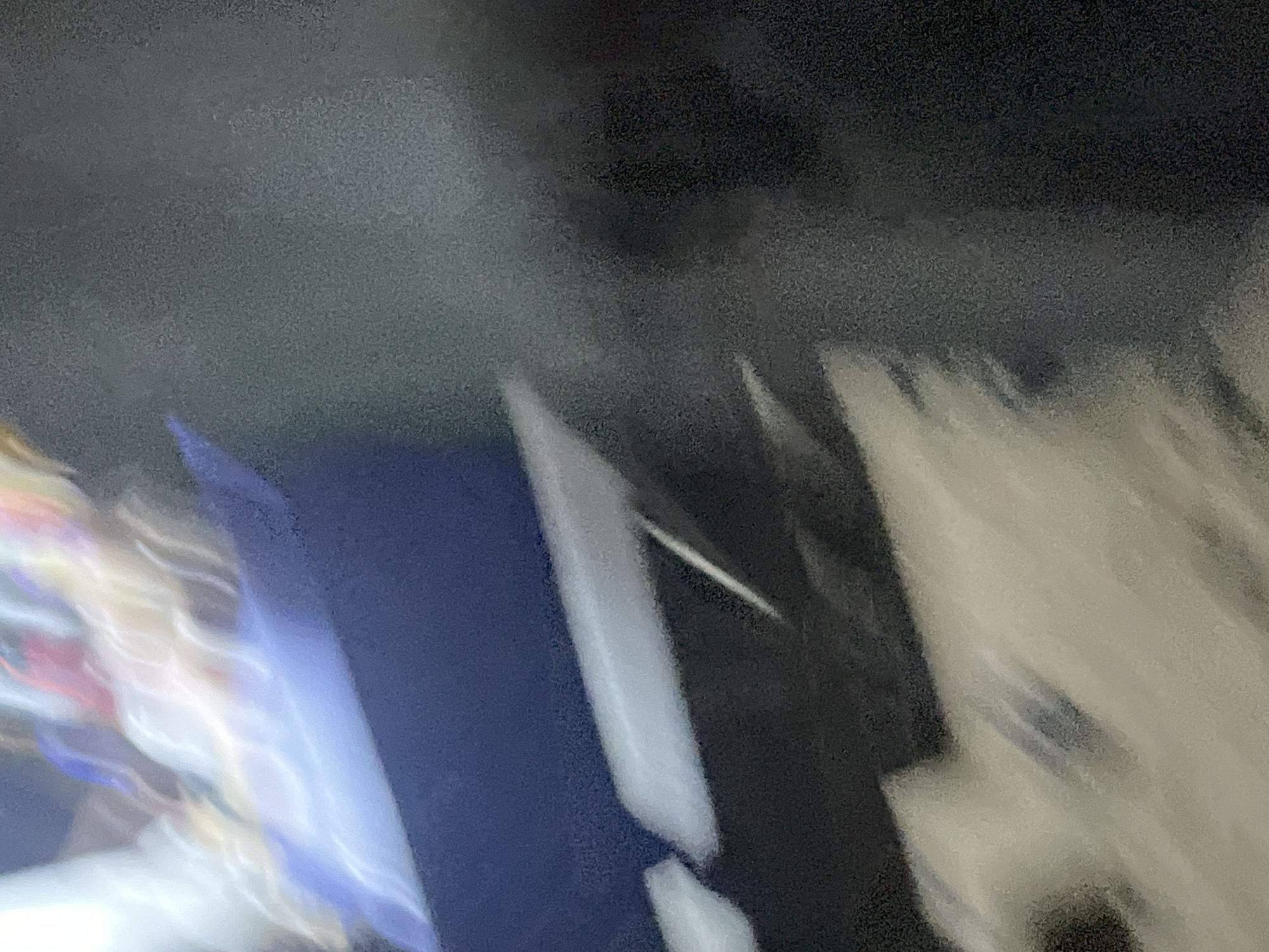The image shows a blurry, abstract scene with streaks of light and dark colors. A dark blue object occupies the middle ground, with lighter-colored, blurred forms above and below it. The background is dark and textured, possibly representing a surface or a dark environment. The motion blur suggests that the image was taken while the camera or the subjects were moving. The scene is abstract and lacks clear identifiable objects or people, making it impossible to determine the location in Lokoja, Nigeria, or any specific details about a crime.