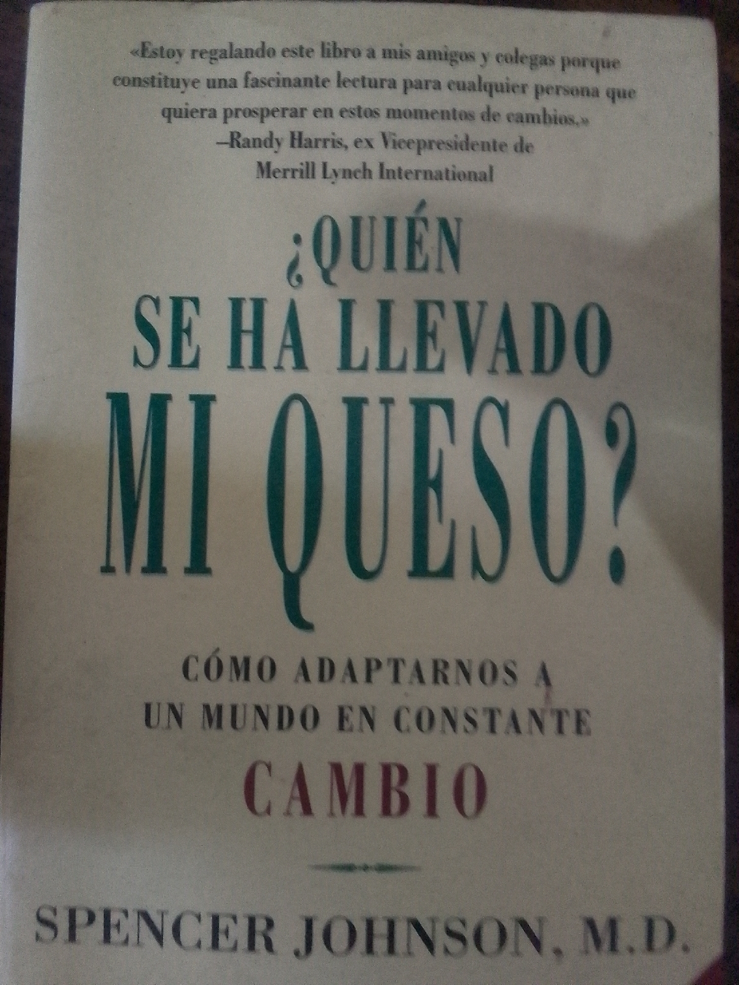 The image shows the cover of the book "¿Quién se ha llevado mi queso?" (Who Moved My Cheese?) by Spencer Johnson, M.D. The title is prominently displayed in large, green text, with the word "CAMBIO" (CHANGE) in red below. Above the title, there's a quote in smaller text attributed to Randy Harris, ex Vicepresidente de Merrill Lynch International. Below the title, it reads "CÓMO ADAPTARNOS A UN MUNDO EN CONSTANTE CAMBIO" (How to Adapt to a World in Constant Change). The author's name, "SPENCER JOHNSON, M.D.", is at the bottom of the cover. There is no evidence this is in Juan Griego, Venezuela.