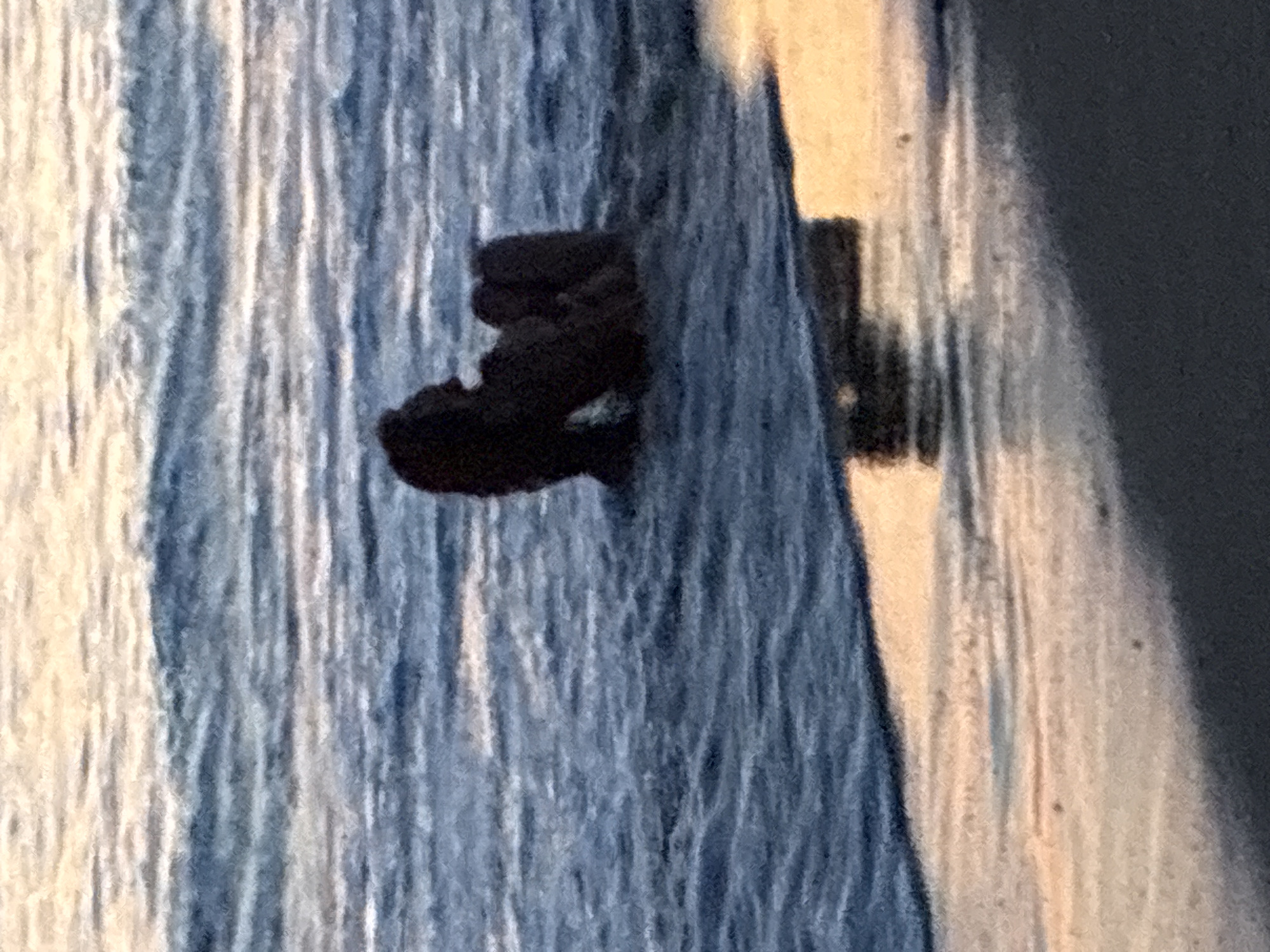 A dark, silhouetted object, possibly driftwood or a dark rock formation, sits in the shallow water near the shore of a beach. The water is choppy with gentle waves, reflecting the soft, warm light of the sunset. The sand in the foreground is wet and catches the orange and yellow hues of the sky. The image is a close-up, focusing on the object and the immediate surroundings. The scene is peaceful and serene, conveying a sense of calm. The location is likely a beach in Alanya, Turkey, given the warm lighting and coastal environment.