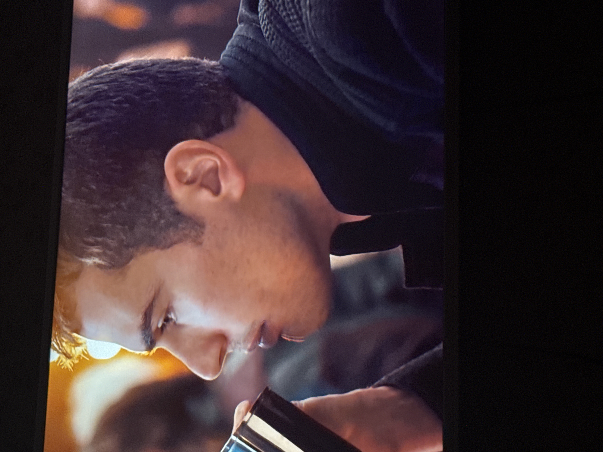 A close-up, tilted shot shows a man with short brown hair and light skin. He is wearing a dark-colored hooded garment, possibly a sweatshirt or jacket. He is looking down at a dark object with a light-colored rim in his hands. The background is blurred. There is no information regarding the location in Mytishchi, Russia.