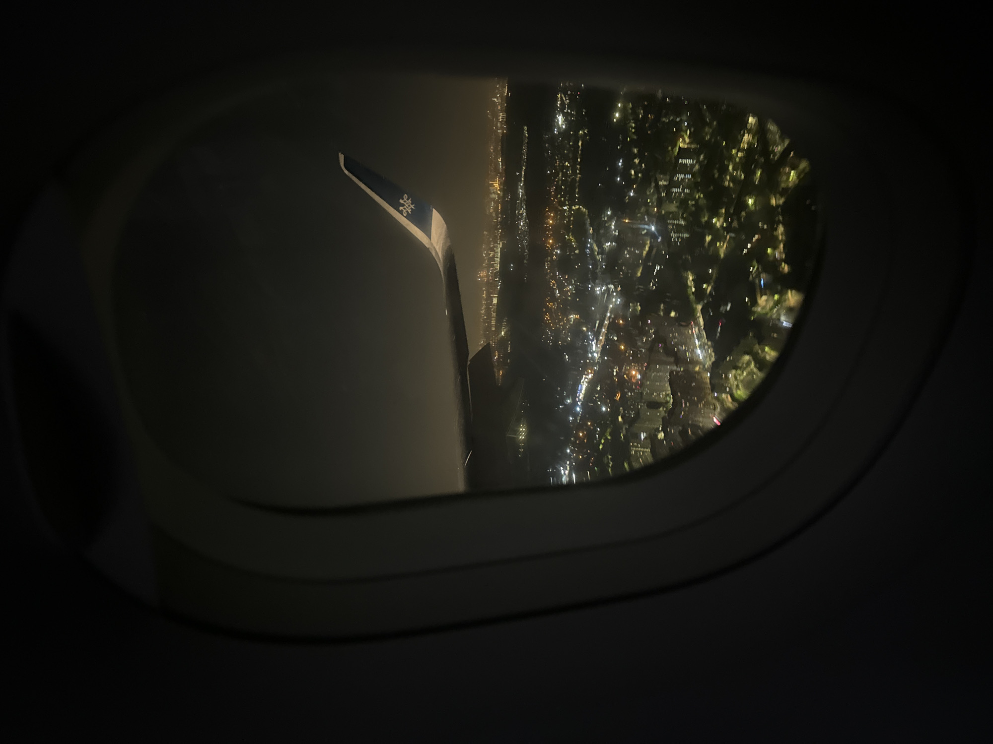 The image shows a view from an airplane window at night. Outside the window, the city lights of Moscow, Russia, are visible, giving the impression of a cityscape seen from above. The wing of the airplane is also partially visible.