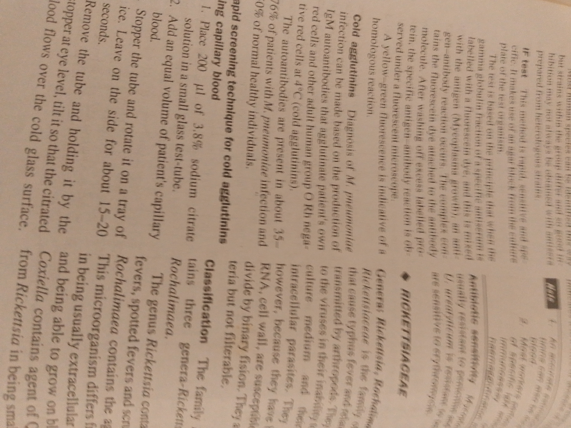 The image displays a close-up, slightly blurry view of a printed document, oriented vertically. The text is primarily in English and discusses medical or biological topics, specifically mentioning "cold agglutinins," "M. pneumoniae," "Rickettsiaceae," and "antibiotic sensitivity." There are also headings like "If test," "Classification," and "RICKETTSIACEAE."
The text suggests a scientific or medical context, possibly from a textbook or laboratory manual, given the detailed descriptions of diagnostic tests and bacterial classification. There are no people, objects, or scenes beyond the document itself. The lighting is somewhat dim, making it difficult to discern specific details like the paper's texture or background. The image quality is moderate, with some parts of the text being sharper than others. The overall impression is of a page from a reference material.