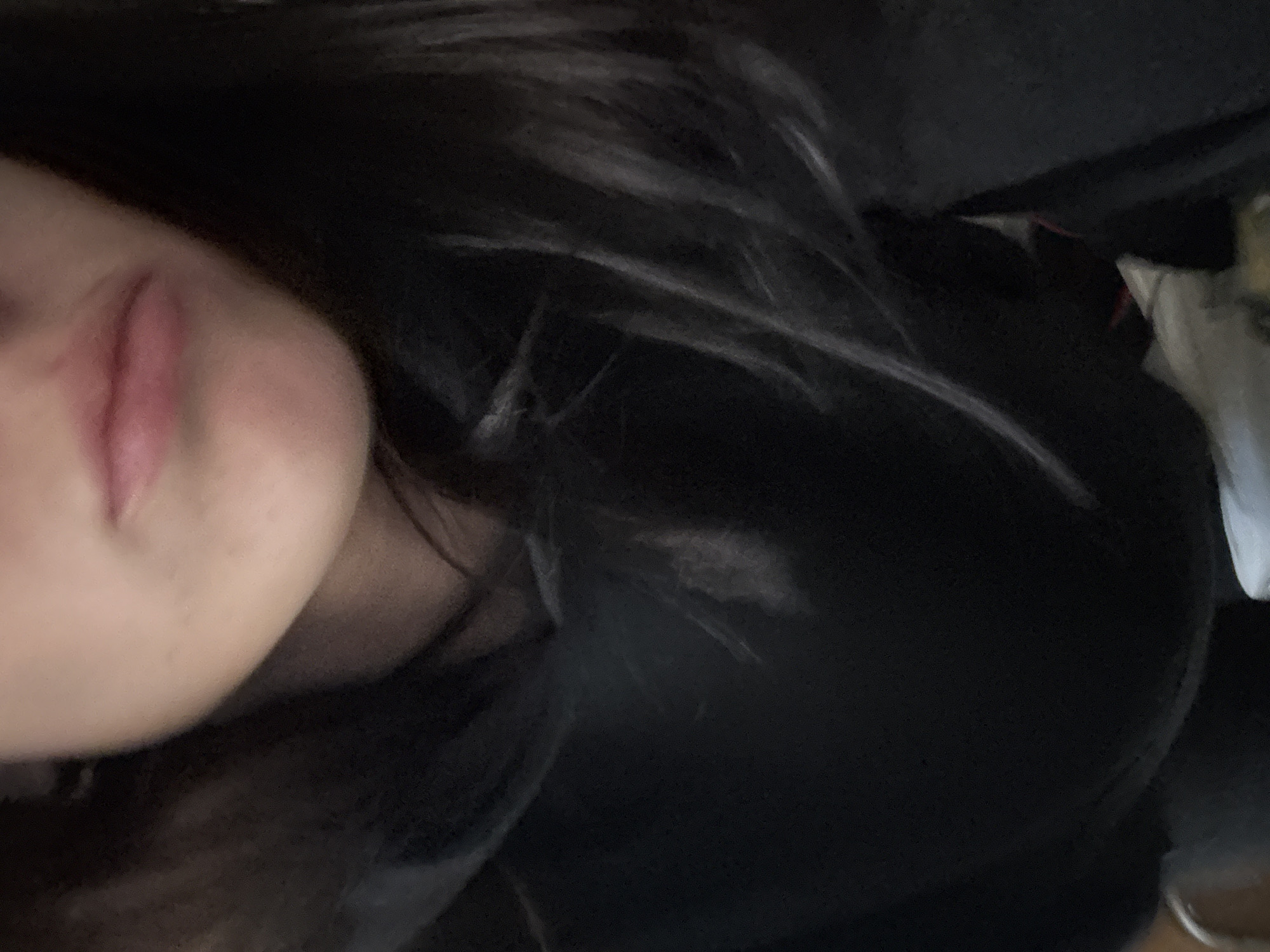A close-up, tilted image shows a person's face, specifically the lower part, including the lips and cheek. The person has dark hair, some strands of which are visible near the face. The person is wearing a dark-colored garment. The background is predominantly dark and out of focus. There is no clear indication of the location being Buenos Aires, Argentina, or any city.