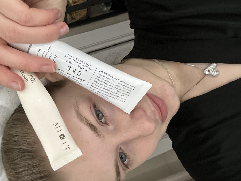 A woman displays two skincare products: Dr. Althea 345 Relief Cream for all skin types, highlighting hydrating and calming effects with ingredients like Ceramide NP and Panthenol, and a MIXIT ONE cream. The Dr. Althea cream promises blemish care with Resveratrol, Tannic Acid, and Niacinamide, alongside nourishing and soothing properties. The woman is lying down, wearing a black top and a silver heart necklace.