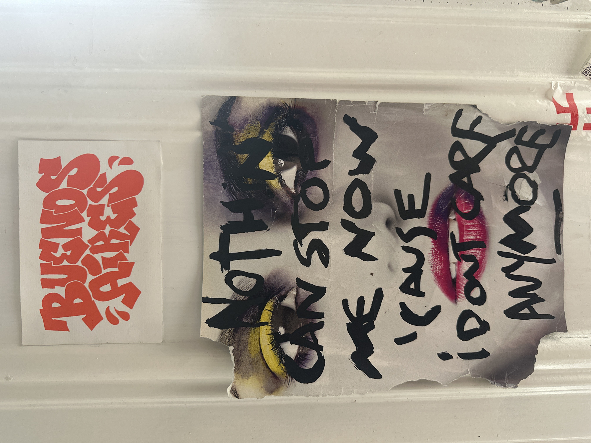 Two stickers are on a white surface. The sticker on the left has orange lettering that reads "BURNS SURFACES". The sticker on the right features a torn image of a face with purple and yellow eye makeup and red lipstick. Black paint covers the image, with visible words including "CAN'T STOP", "NOW", "CAUSE I DON'T CARE", and "ANYMORE". The location in Buenos Aires, Argentina is undetermined.