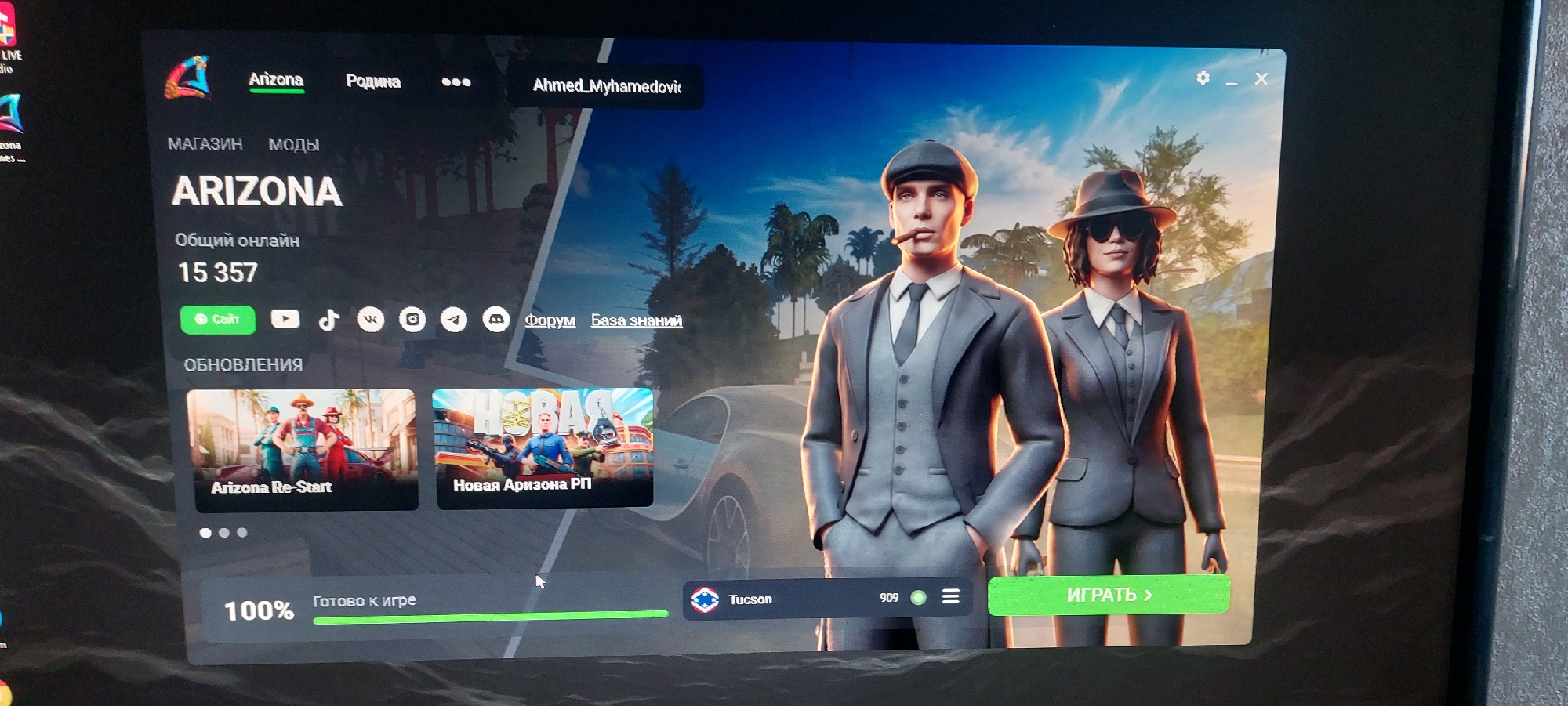The image shows a computer screen displaying the game launcher for "Arizona RP" (Arizona Roleplay), a popular Grand Theft Auto V roleplay modification. The launcher features the game's title prominently, along with the current online player count, which is 15,357. Below this, there are icons for social media platforms and links to the game's website, forum, and knowledge base. The background features artwork of two characters dressed in vintage suits and hats.
Further down the screen, there are sections for game updates and news, with two prominent game modes displayed: "Arizona Re-Start" and "Новая Аризона РП" (New Arizona RP). A progress bar at the bottom indicates that the game is 100% "Готово к игре" (Ready to play), and the selected server is "Tucson".
There is no information within the image to suggest any connection to the city of Oral, Kazakhstan. The visual content is entirely related to the video game and its interface.