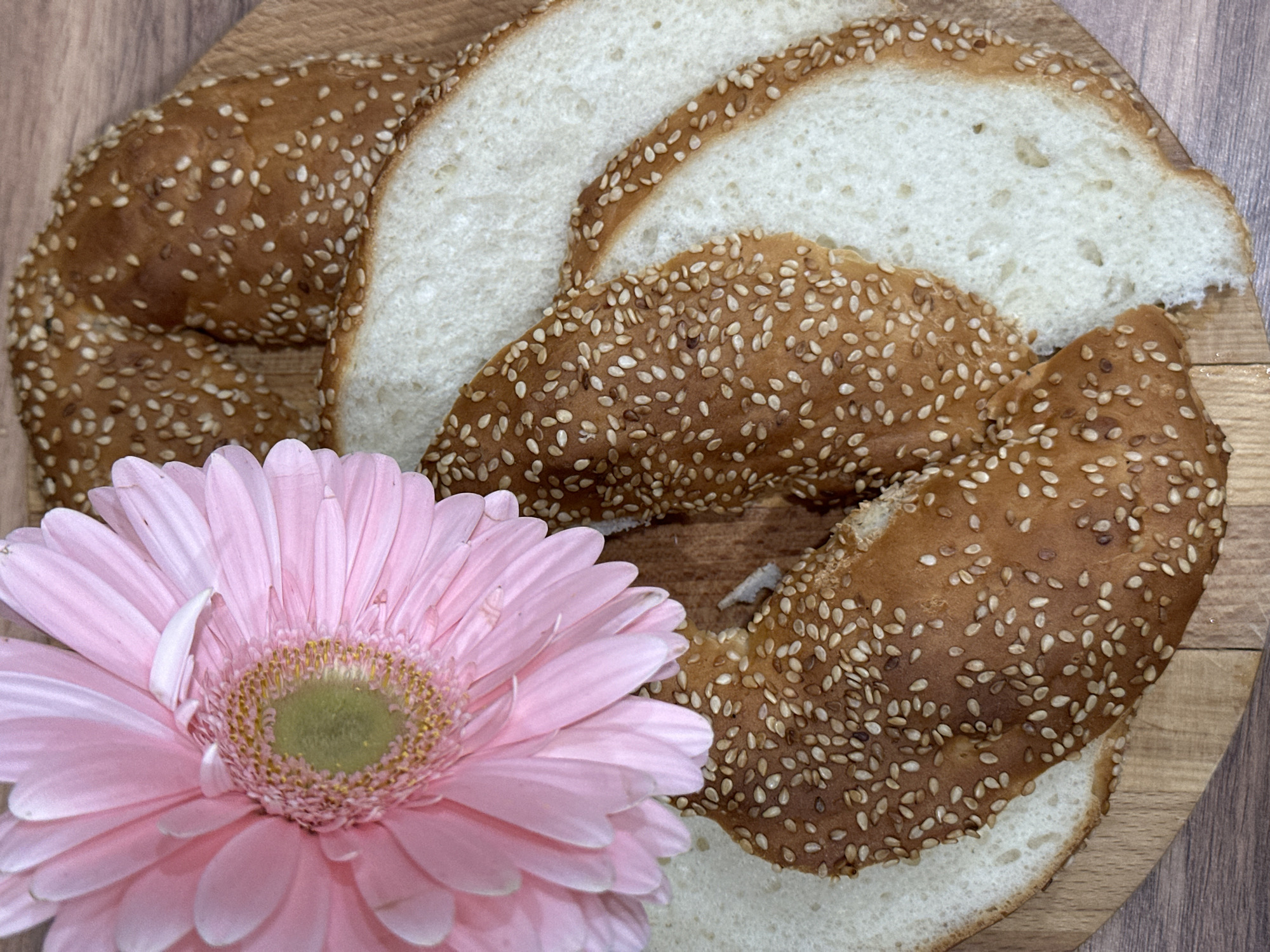 The image shows slices of a sesame-seed crusted bread arranged on a wooden surface, likely a cutting board. A pink gerbera daisy is positioned prominently in the lower left portion of the image, partially obscuring the bread. The location, Kazan, Russia, is not discernible from the visual information provided.