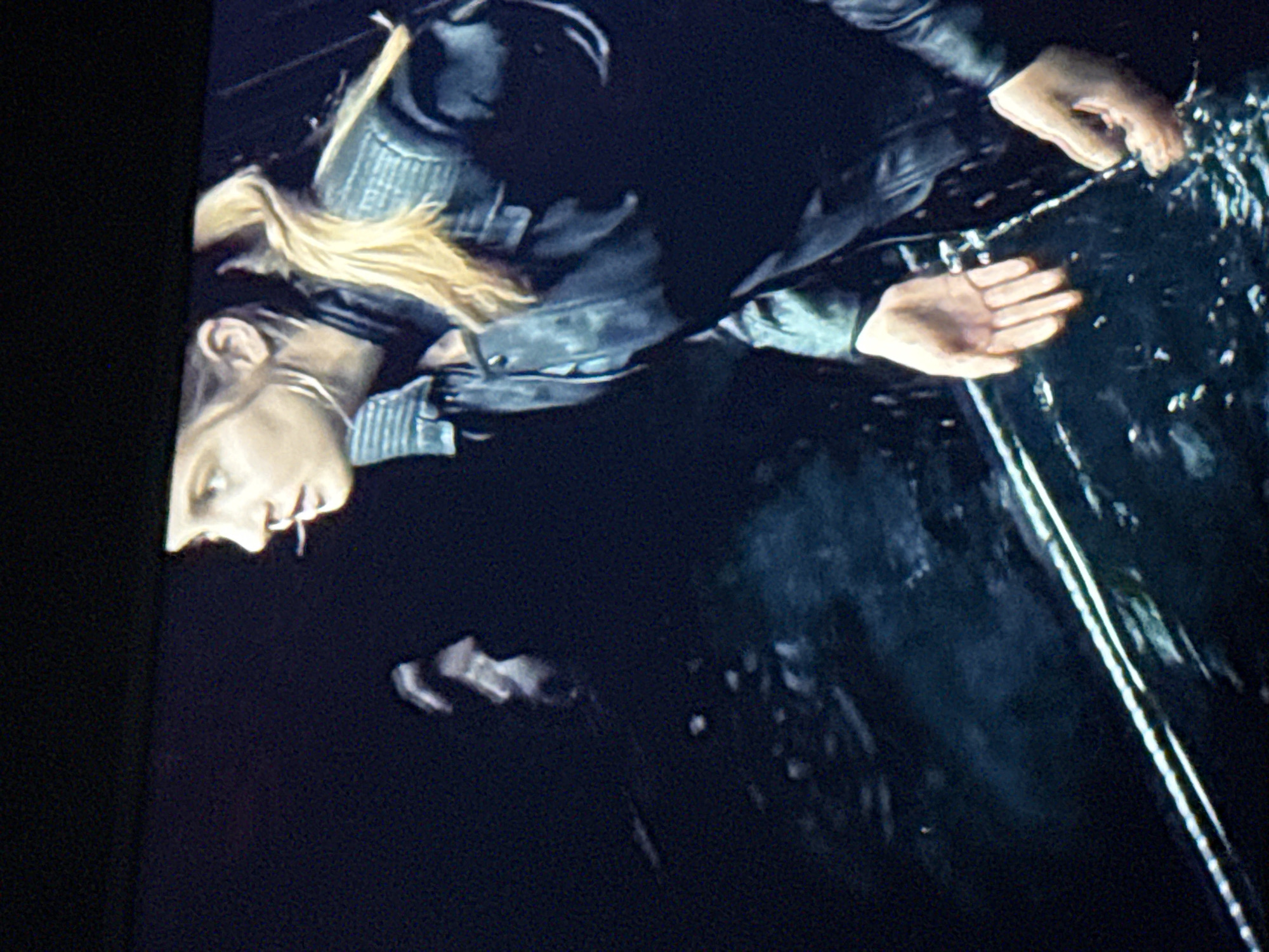 A woman with blonde hair wearing a black leather jacket is touching a reflective surface, possibly water or glass. Her reflection is visible in the lower portion of the image. The surrounding environment is dark, with a dark background surrounding the reflection. There is no evidence to determine that this image was taken in Mytishchi, Russia.