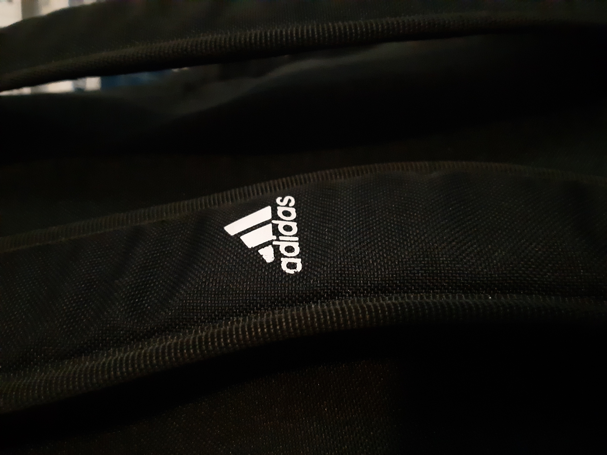 A close-up shot focuses on a black Adidas backpack. The Adidas logo, consisting of the three slanted bars and the company name, is prominently displayed in white. The backpack appears to be made of a textured fabric. The image does not provide enough context to determine a specific location in Plovdiv, Bulgaria.