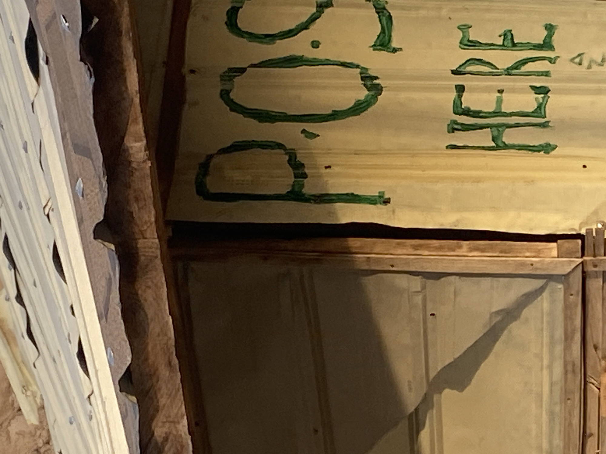 An exterior shot shows a corrugated metal roof with a wooden overhang. On the wall beneath the overhang, the words "POS HERE" are written in green paint. To the left, a windowpane reflects a shadow. The location is identified as Jauro Yinu, Nigeria.