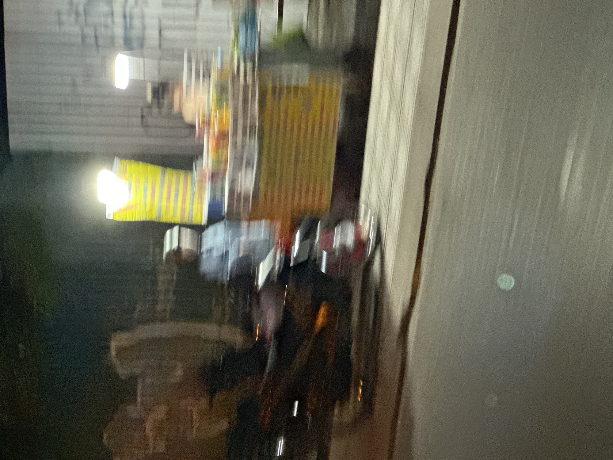 The image depicts a blurry scene, likely taken at night in Bac Nha Trang Ward, Vietnam. Visible are a motorcycle, a food stall illuminated by lights, and a building. The scene appears to be captured in motion, making details unclear.