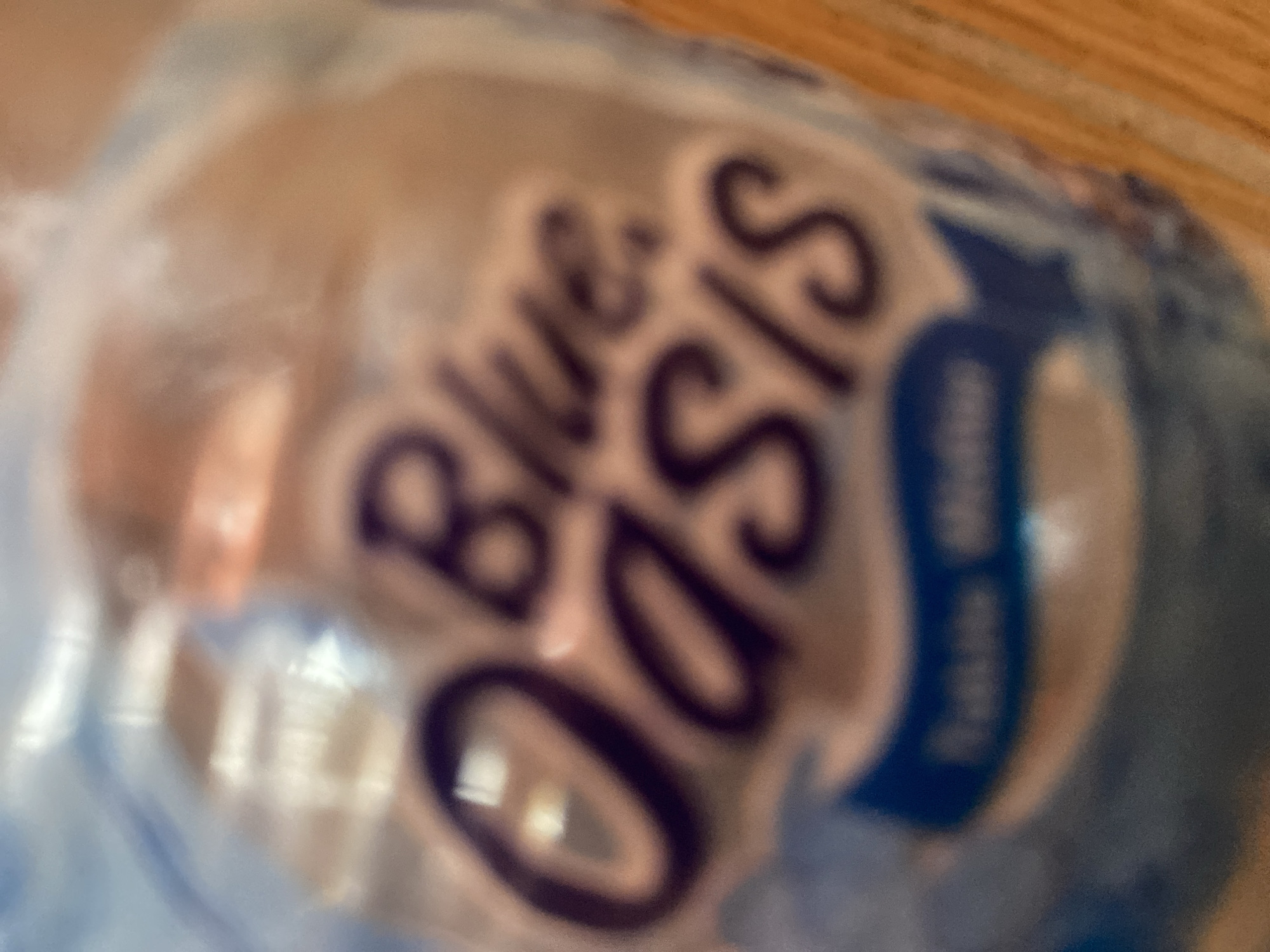 The image shows a close-up, out-of-focus view of a plastic bottle of Blue Oasis table water. The bottle has a blue label with the brand name "Blue Oasis" in dark purple lettering. The text "Table Water" is also visible on a blue band at the bottom of the label. The bottle appears to be sitting on a wooden surface. No specific location in Jalingo, Nigeria is identifiable.