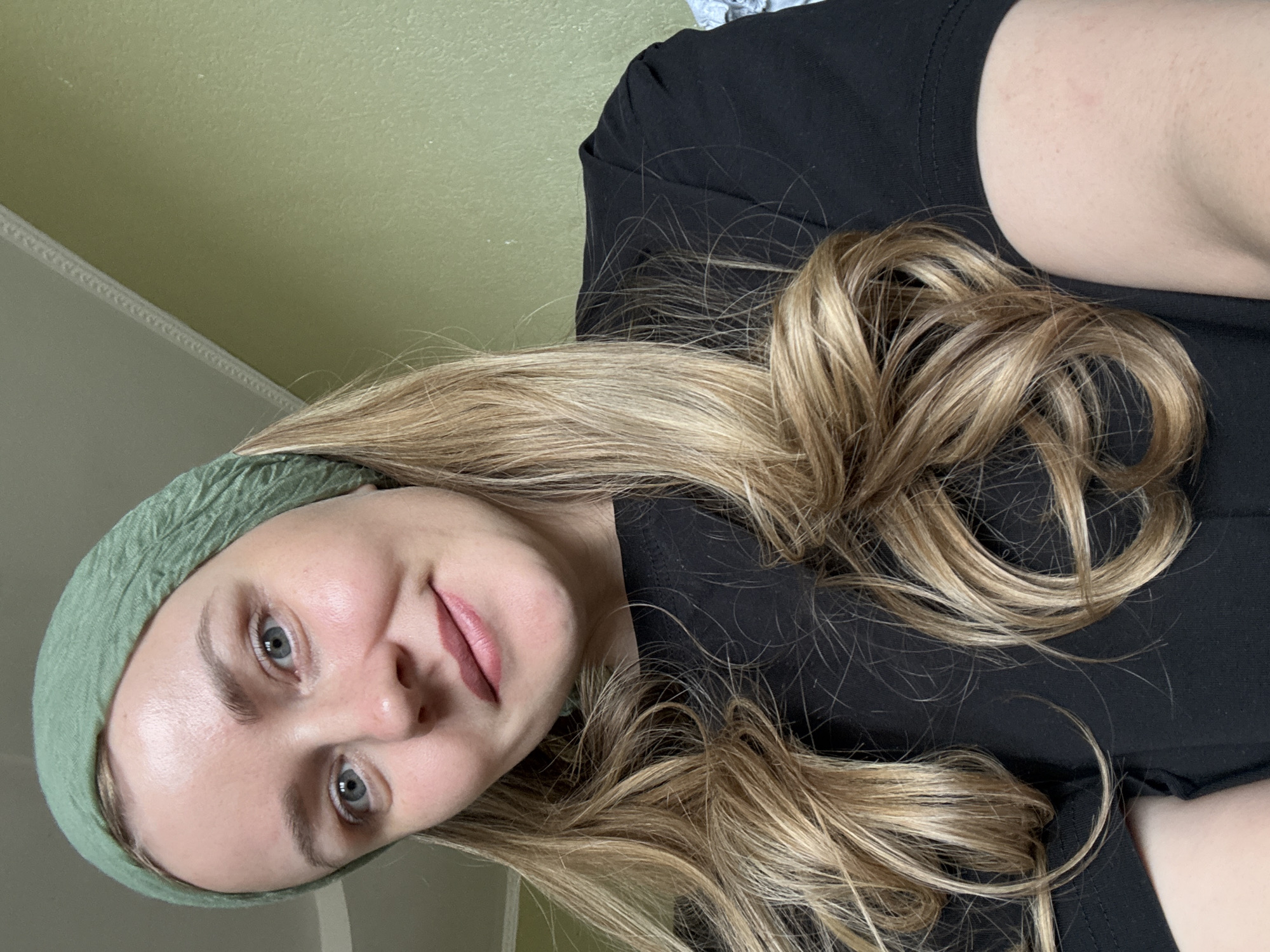 A woman with fair skin and long, blonde hair is shown in a close-up, selfie-style image. She is wearing a light green headscarf. The woman's eyes are blue-gray. She is wearing a black top. The background appears to be a light green wall and a portion of a white door. The location in Chaikovsky, Russia, cannot be determined from the image.