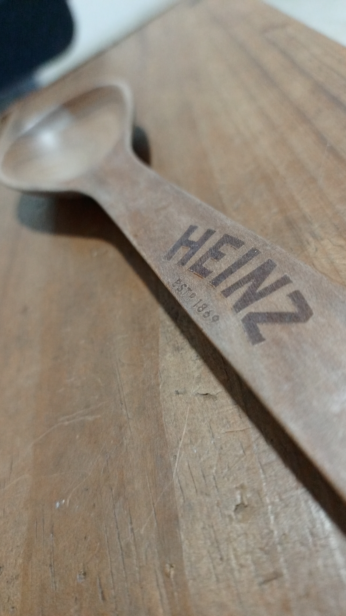 A close-up shows a wooden spoon with the "HEINZ" logo and "ESTD 1869" engraved on the handle. The spoon rests on a wooden surface, possibly a cutting board or table. There's nothing to indicate the location is Los Robles, Venezuela. There are no people present.