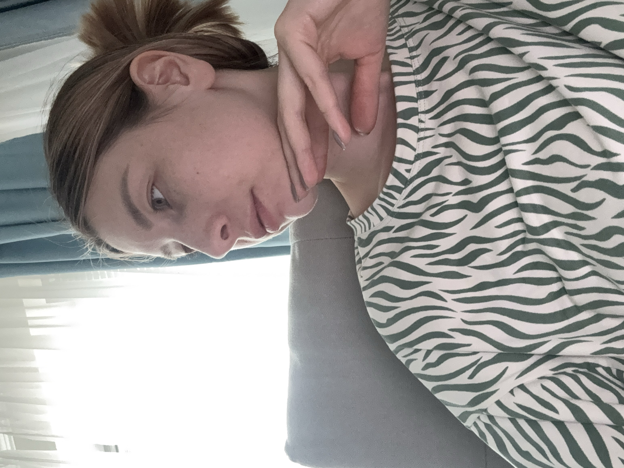 A young woman is positioned in front of a window. She is wearing a green and white striped shirt. Her hair is in a messy bun. Her hand is touching her face. The image is taken indoors with bright light streaming in from the window. No indication of location in the city of Moscow, Russia.