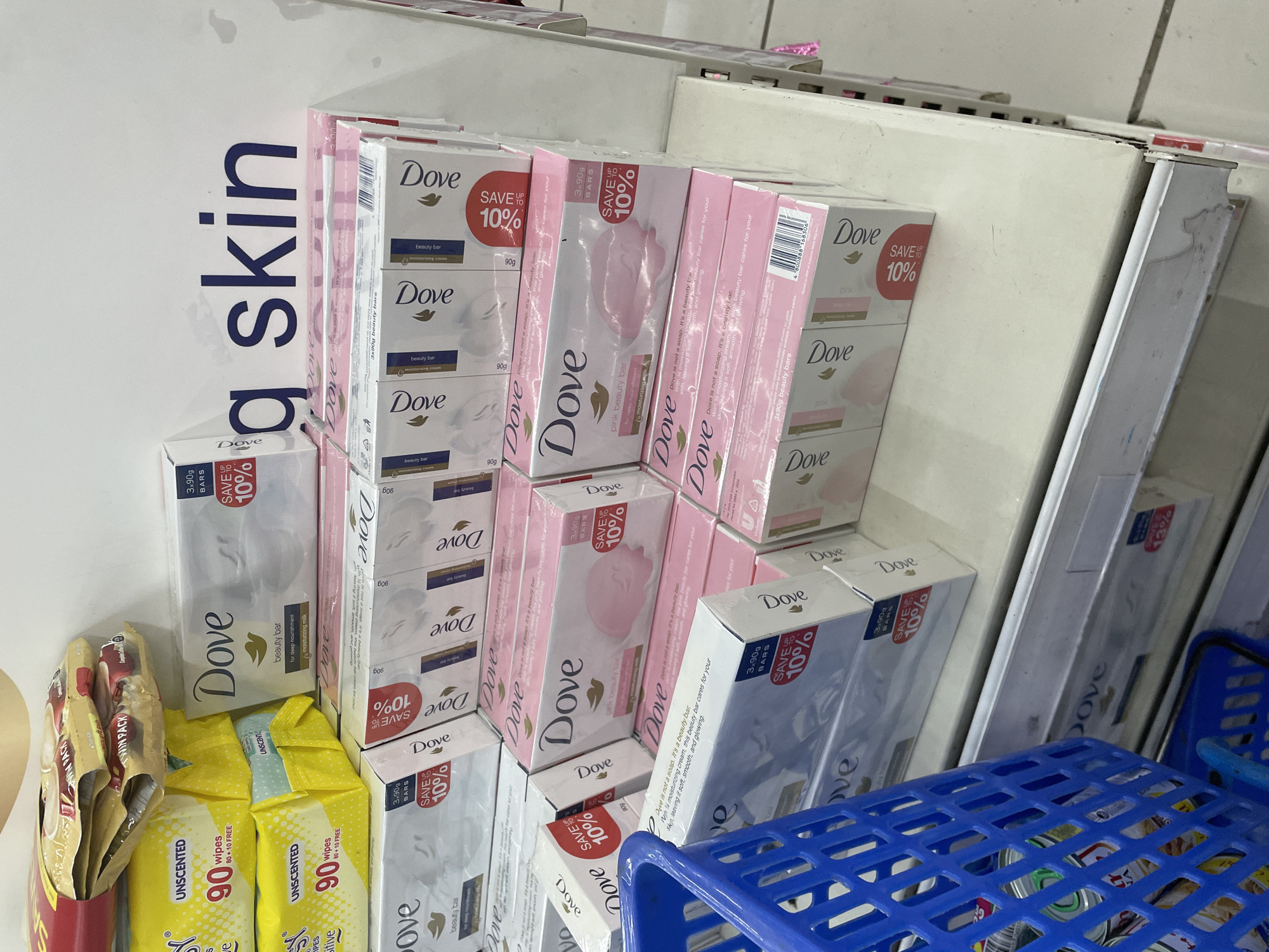 The image depicts a retail shelf stocked with Dove beauty bars and baby wipes. In the foreground, a blue plastic shopping basket is visible. The shelves are white and appear to be in a store environment. The products are arranged in neat rows. Above the products, a blue text on a white background reads "g skin". This suggests the context of a beauty or personal care product display. Without additional information or context, the specific location within Davao City, Philippines, cannot be determined from the image itself. The scene is well-lit and appears to be an indoor retail setting. There are no people visible in the image.
