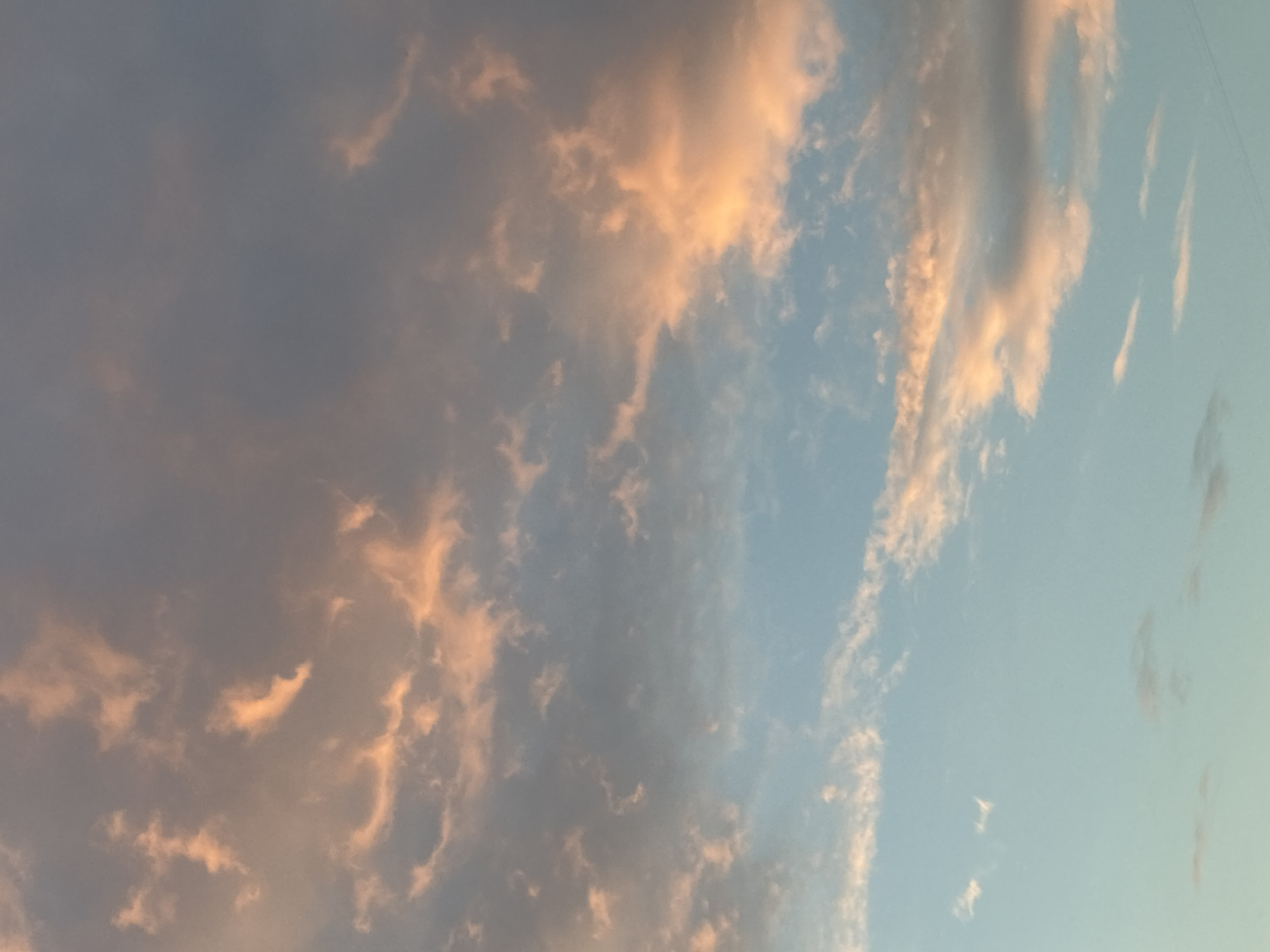 The image shows a sky filled with clouds. The clouds range in color from a light blue-gray to a darker gray, with some tinged with a peach or light orange hue, likely from the sun. There is no visible city, people, subjects, or objects. The environment is a sky at dusk or dawn. Moscow, Russia, is not discernible from the image.