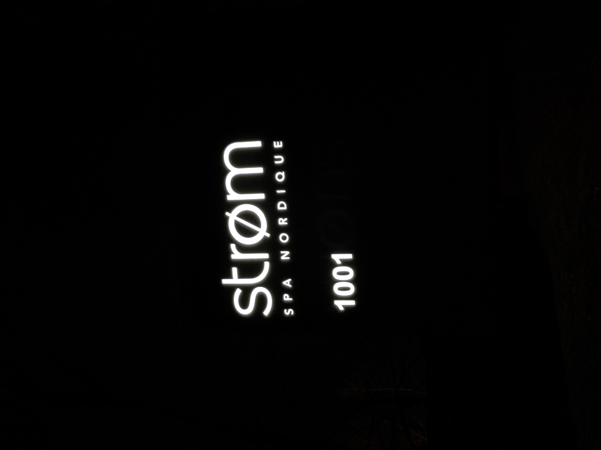 A nighttime shot of a vertical sign that reads "strøm SPA NORDIQUE 1001" in white lettering. It is a storefront in the city of Montreal, Canada.