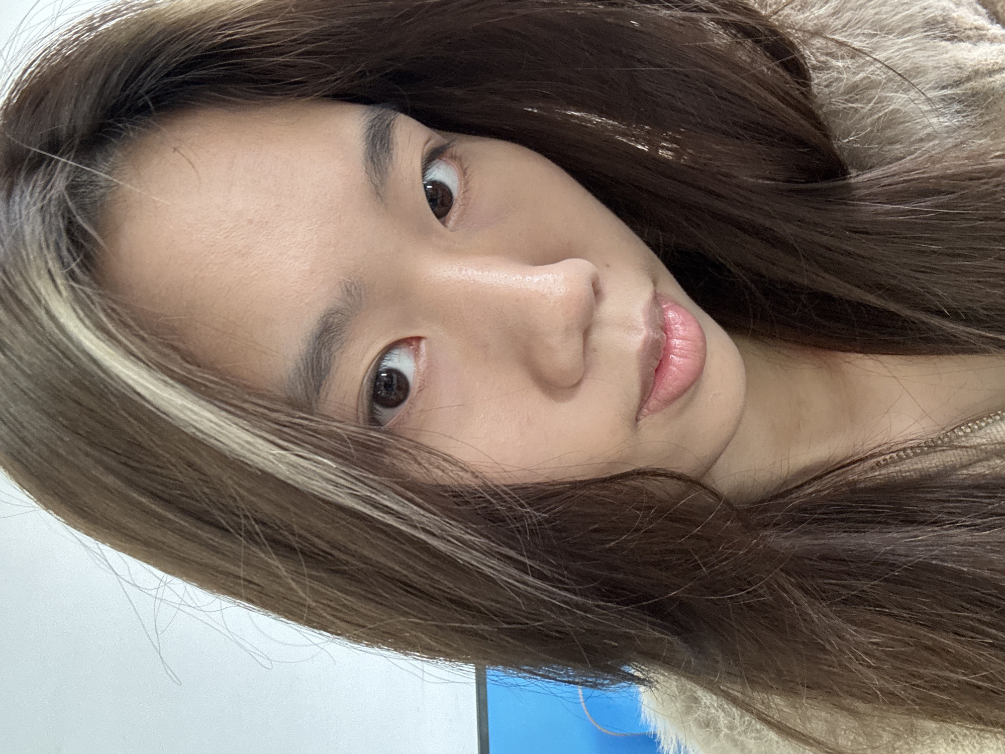 A selfie of a young East Asian woman with long brown hair, featuring a light-colored streak on one side. Her eyes are brown and she has a fair complexion. The background is a light blue and white wall. There's no visible information indicating this photo was taken in Nan'an District, China.