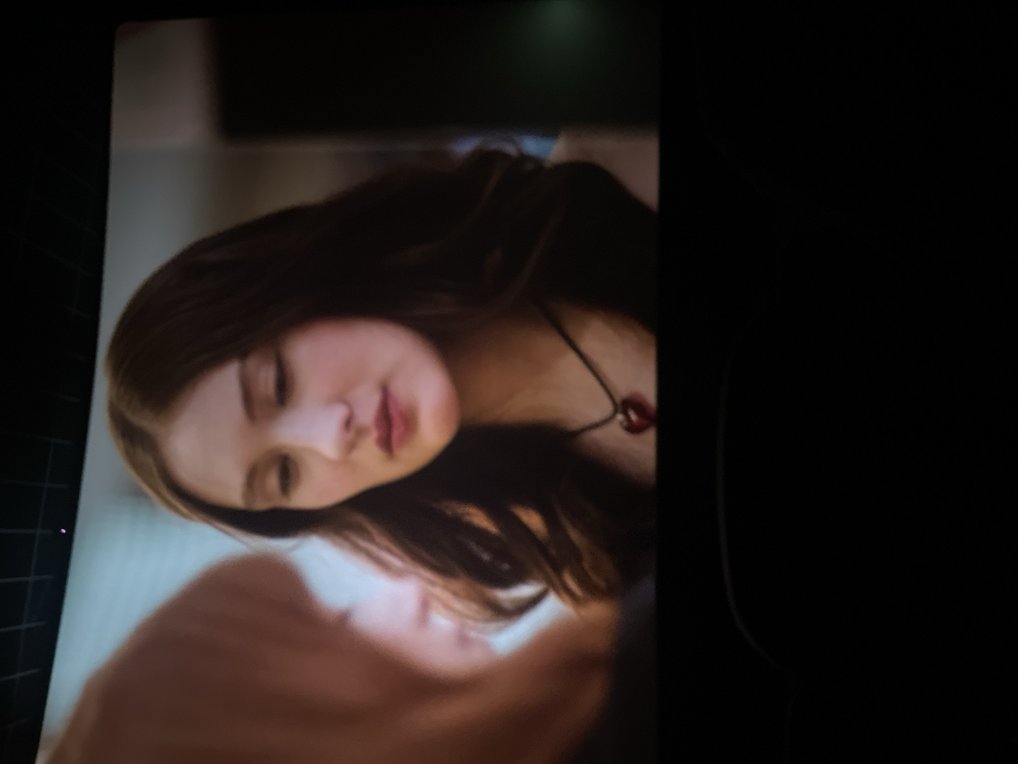 A woman with brown hair is shown in the image. She is wearing a necklace with a dark red pendant. The scene appears to be indoors and illuminated by artificial light. There is another person whose face is partially visible in the bottom portion of the image. The image does not provide enough information to determine the exact location in Saint Petersburg, Russia.