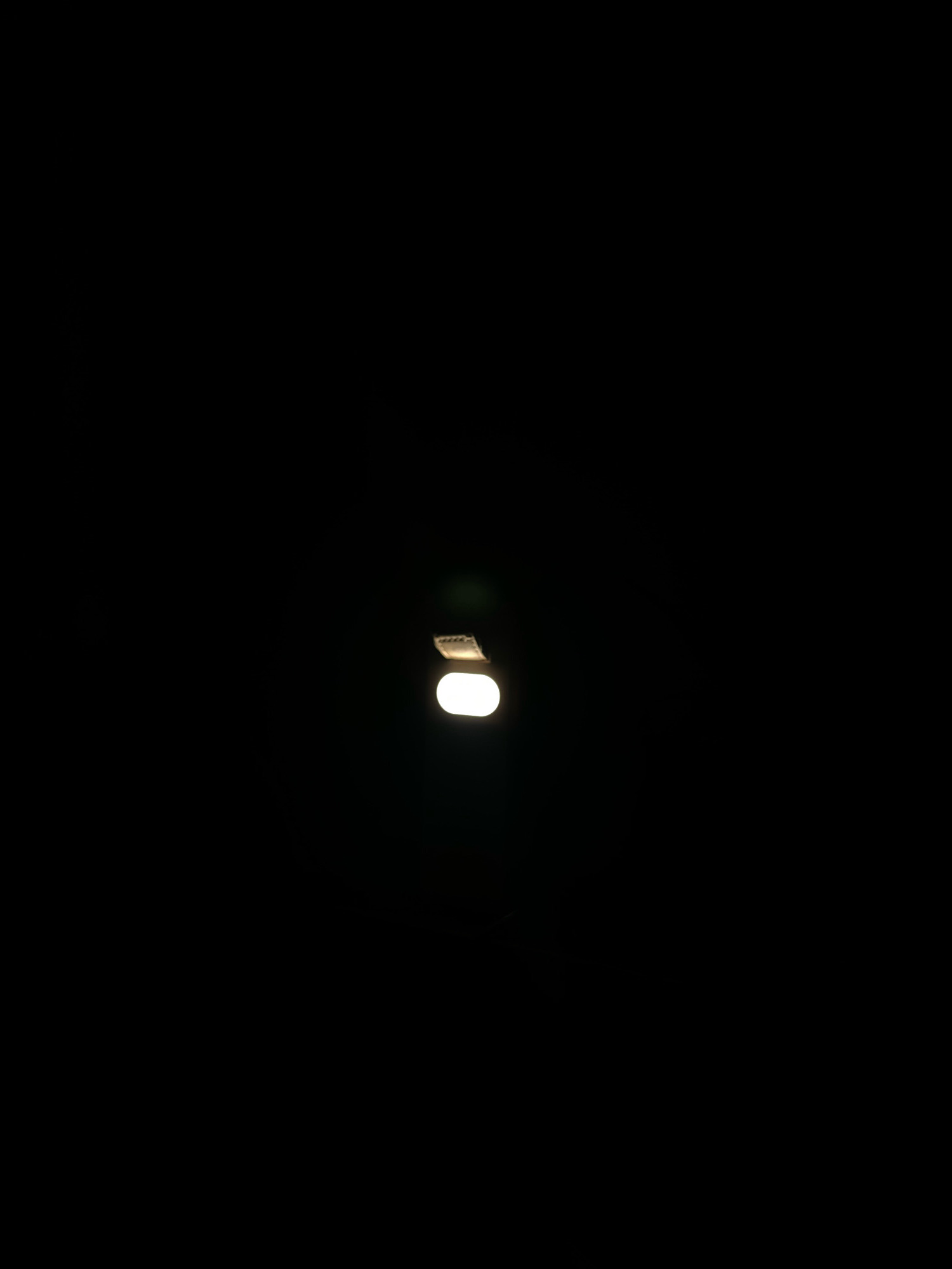 The image shows a close-up shot of a street light at night, casting a bright, white glow against the blackness of the sky. The light fixture itself is partially visible at the top of the frame, appearing metallic and weathered. The overall impression is one of isolation and stillness, with the solitary light drawing the viewer's attention to its luminescence. This scene could be representative of many urban environments in Umuahia, Nigeria, where streetlights illuminate the darkness and provide a sense of order and safety amidst the night.