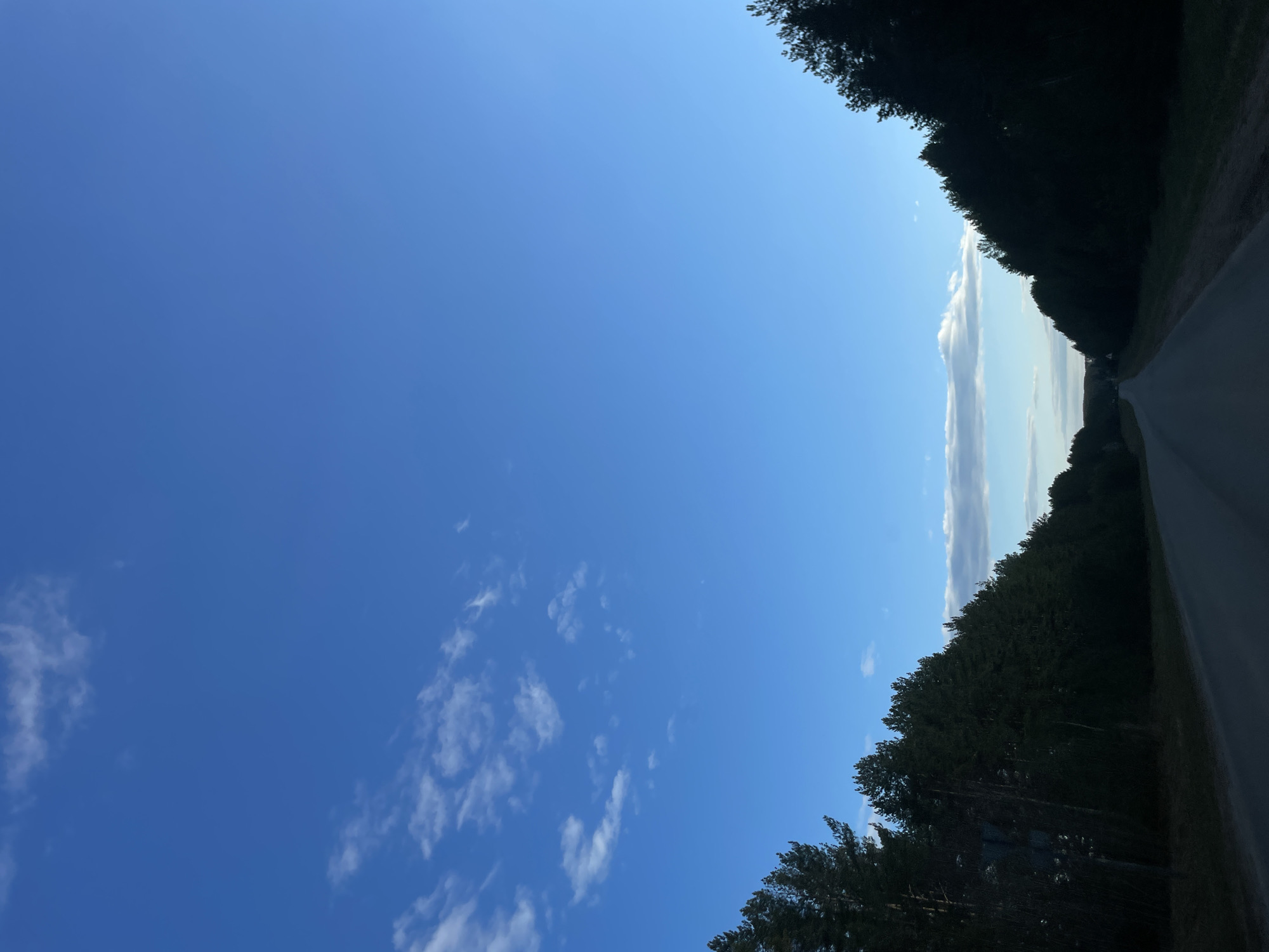 The image shows a road surrounded by trees under a blue sky with scattered clouds. The location is Средний Постол, Russia.