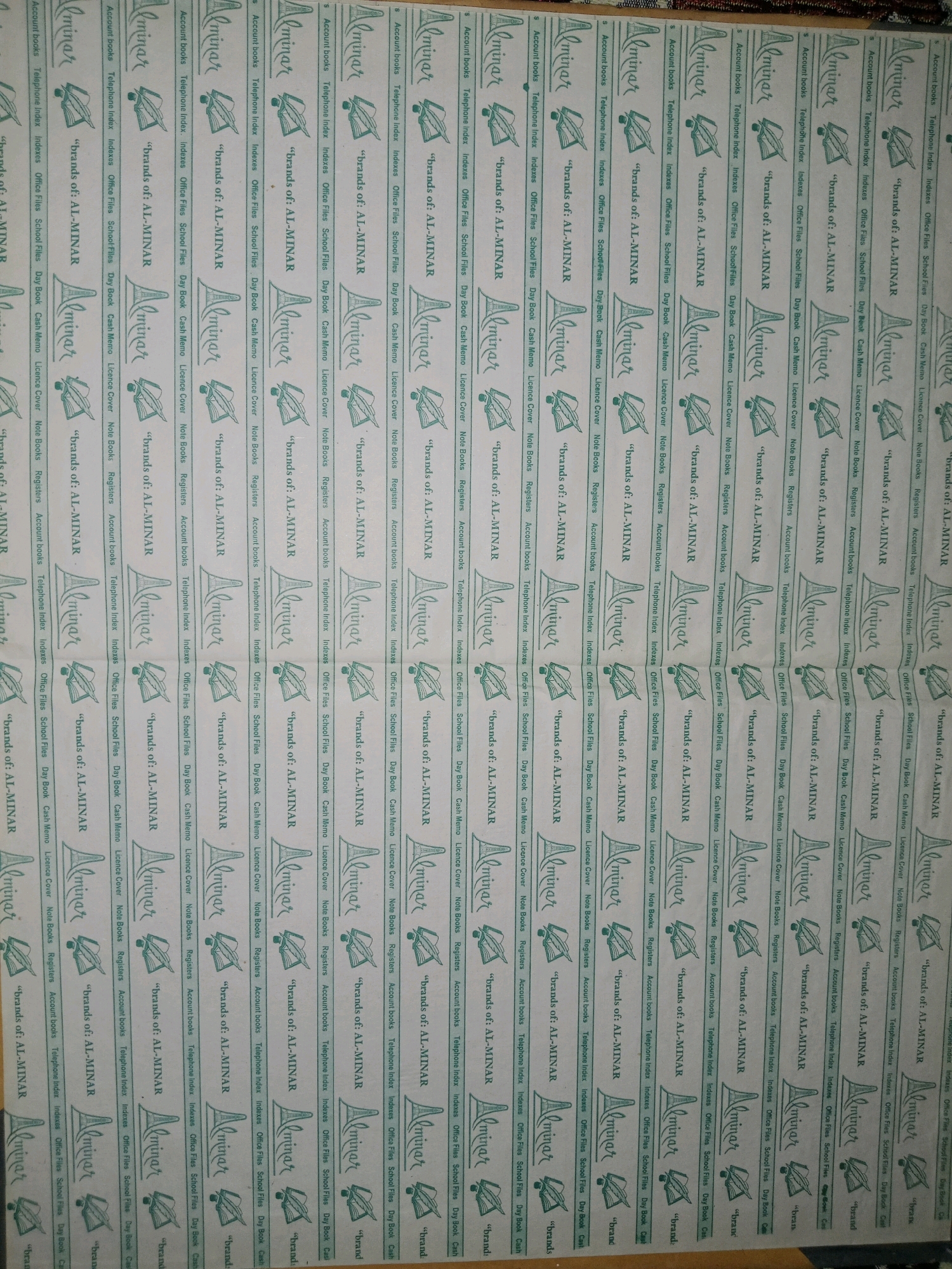 The image displays a repeating pattern of branding for "Al-Minar" products, which are stationery items. The branding consists of the stylized "Al-Minar" signature, an illustration of an open book with a quill and inkwell, and a list of stationery products. The list includes: "Account books, Telephone index, Indexes, Office Files, School Files, Day Book, Cash Memo, Licence Cover, Note Books, Registers." This branding is repeated horizontally across a light-colored background. The overall impression is that of a roll of paper or a packaging material for stationery products. The image does not provide any visual information about the city of Bahawalpur City Tehsil, Pakistan, nor does it depict any people, actions, or interactions. It is purely a commercial design element.