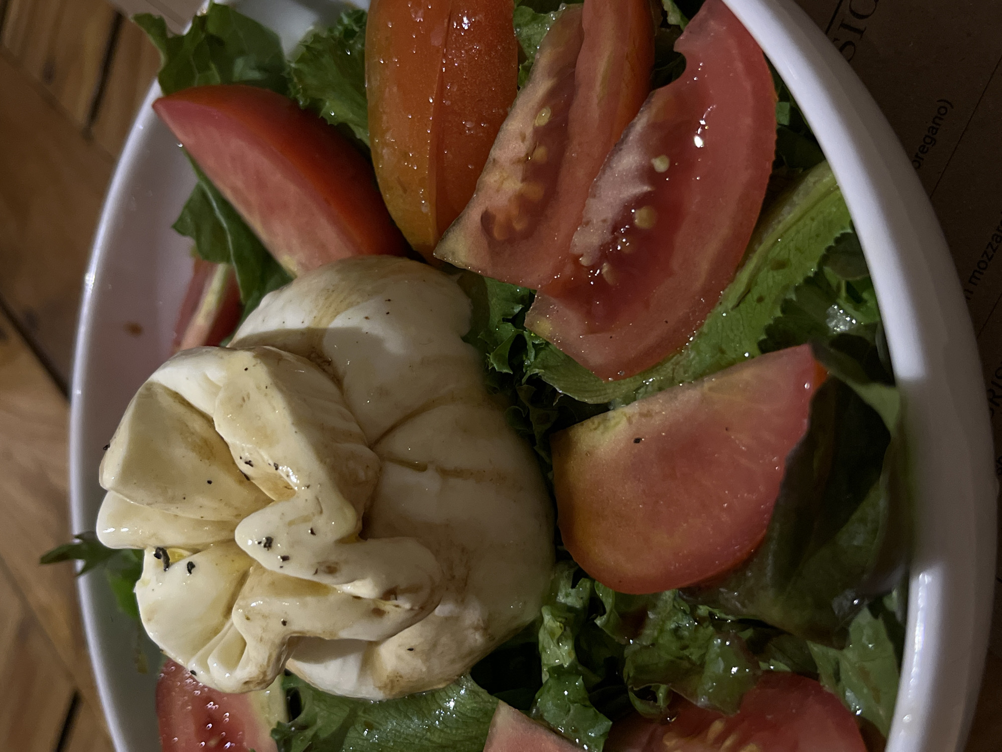A close-up, top-down shot depicts a salad in a white bowl, featuring slices of red tomatoes, fresh green lettuce, and a central, creamy-white ball, possibly a type of soft cheese. The components are arranged in a visually appealing manner. The scene appears indoors. Although the city of Galle, Sri Lanka, is mentioned, no specific location details are visually present in the image to verify this claim. There are no people visible, and the focus remains solely on the salad.