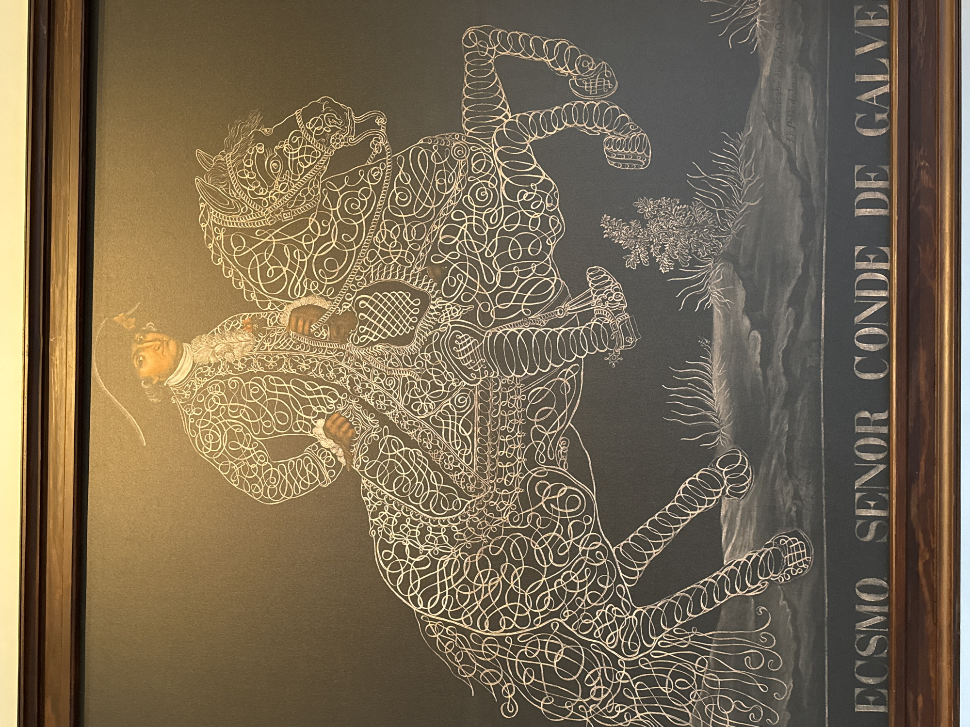 A framed print depicts a man on horseback in a stylized, ornate design. The figures of the man and horse are formed from intricate, looping lines. The man is wearing a detailed outfit, and the horse has decorative elements on its harness. In the background are some stylized plants. A frame borders the print. On the right side of the print, a title reads "ECSMO SENOR CONDE DE GALVE." This image likely originates from Mexico City, Mexico.