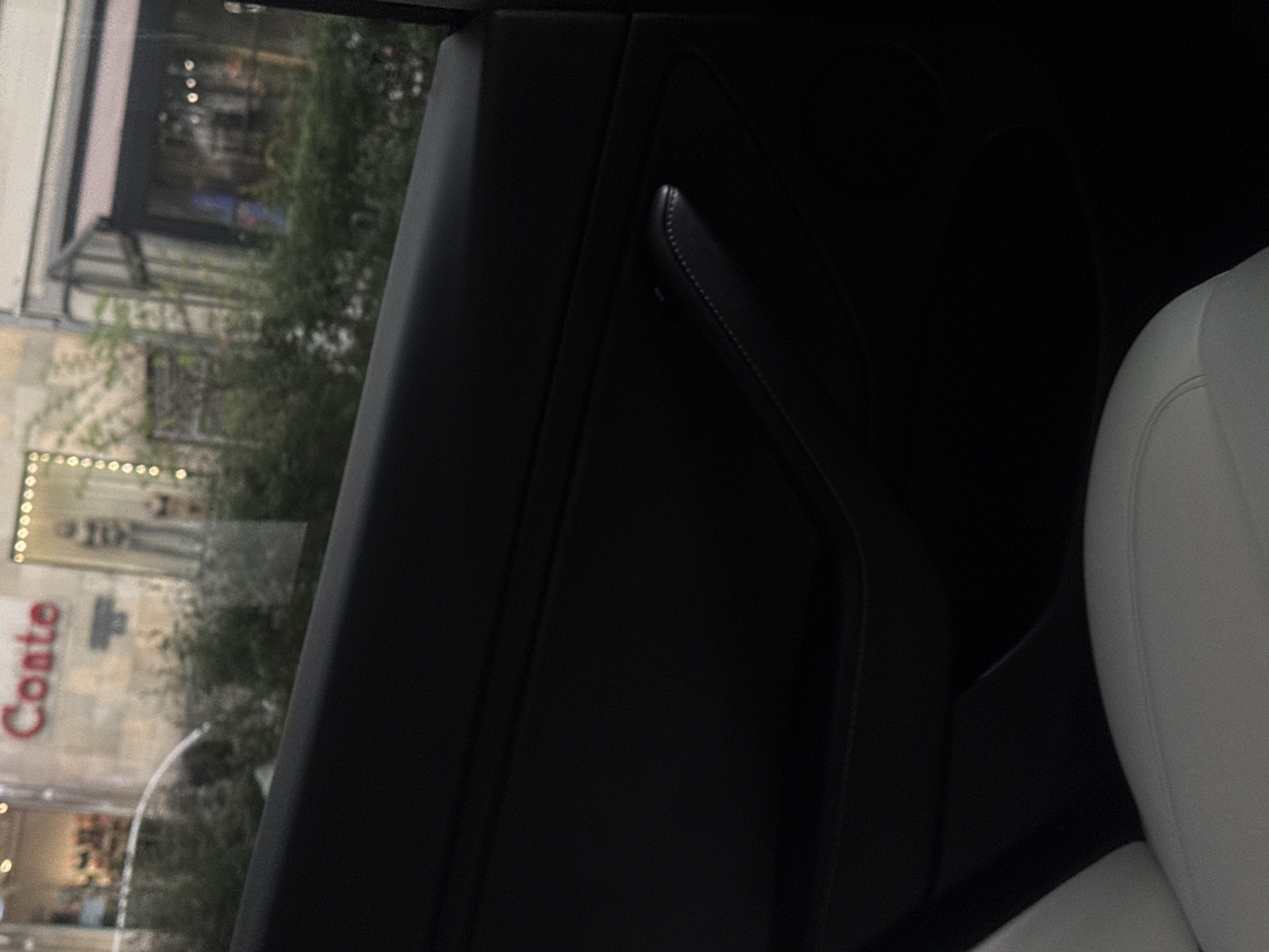 The image depicts an interior view from a car in Yerevan, Armenia. Visible through the car window is a building exterior with the word "Conte" prominently displayed. The car's interior features a black door panel and a white seat. No people are directly visible in the image.