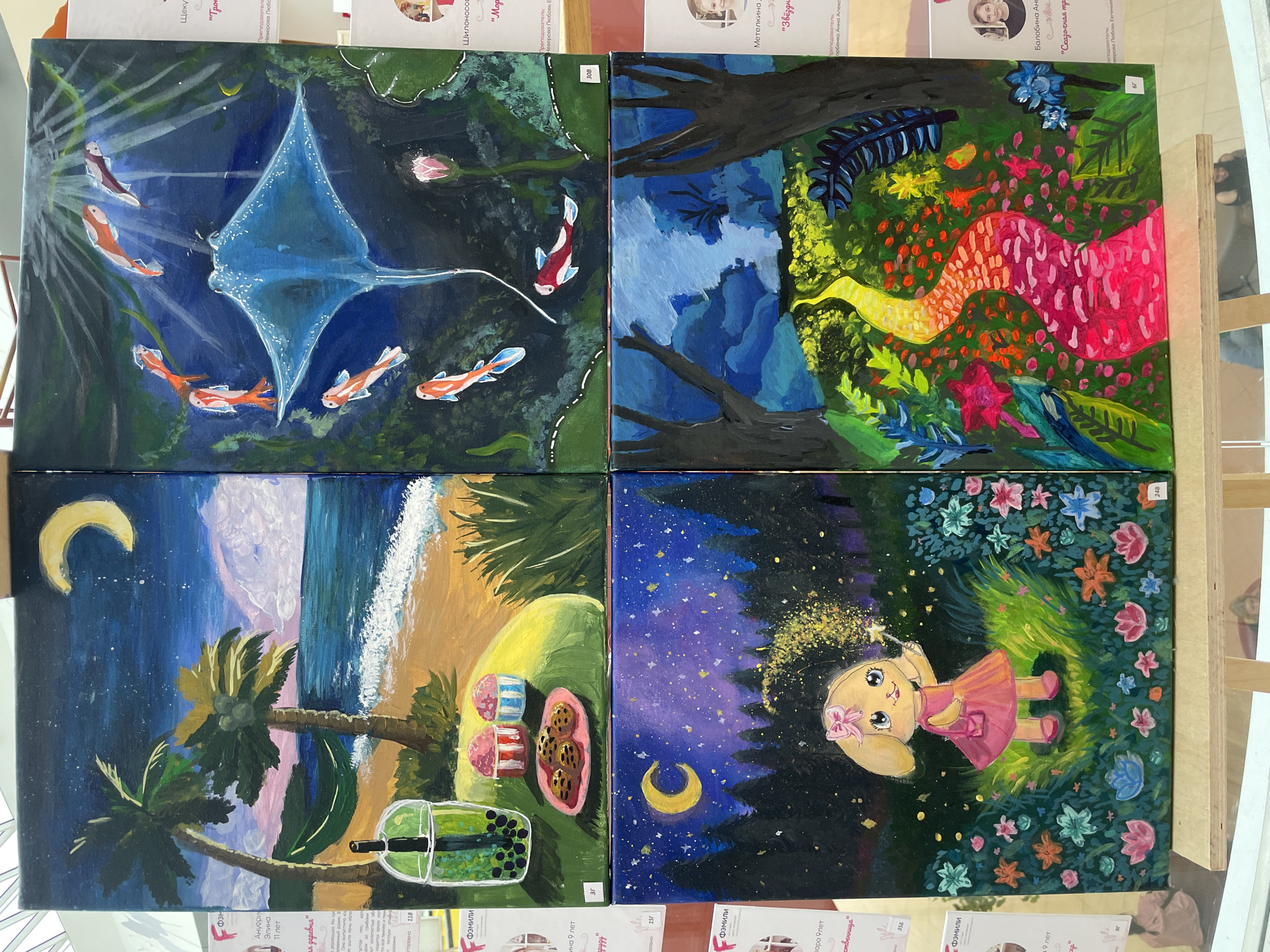 This media file displays a collection of four acrylic paintings, likely from an exhibition, as suggested by the numbered tags and surrounding informational material with Russian text.
The top-left painting depicts an underwater scene with a large blue manta ray swimming gracefully, surrounded by several small, orange and white fish. Sunlight filters down from above, illuminating the aquatic environment with hints of green foliage and a single pink lotus flower. The overall mood is serene and mysterious.
The top-right painting portrays a vibrant, abstract landscape. A dark, imposing tree trunk dominates the foreground, reaching into a dense forest. The background bursts with a riot of color, featuring a winding path or river in shades of yellow, orange, and pink, interspersed with lush green foliage and brightly colored flowers. This painting evokes a feeling of fantasy and wonder.
The bottom-left painting captures a tropical beach scene at dusk. Two palm trees lean over a sandy shore, where the gentle waves of the ocean meet the land. A crescent moon hangs in the deep blue, star-speckled sky, reflecting in the water. In the foreground, there are desserts and a drink, suggesting a relaxing evening.
The bottom-right painting is a whimsical depiction of a young girl in a pink dress standing in a magical forest at night. She holds a wand, from which sparkles emanate. The dark forest is illuminated by a starry sky and scattered bioluminescent flowers, creating an enchanting and dreamlike atmosphere. A crescent moon is also visible in this painting.
The visible Russian text includes names like "Ануфри Элина", "Шилоносов", "Метелкина", "Балабина Аня", and phrases such as "11 лет", "19 лет", "Сказочная страна", and "Звездный час". The context suggests these are likely artist names, ages, and titles of the artworks. The presence of "Фэмили" and "Пермь" on some of the surrounding materials further indicates a connection to Perm, Russia.