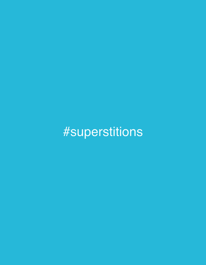 The image displays a uniform, solid teal-blue background. Centered horizontally and vertically on this background is the white text "#superstitions". No individuals, physical objects beyond the text, actions, interactions, or specific environmental details, including any location within the city of Ado, Nigeria, are depicted within the frame.