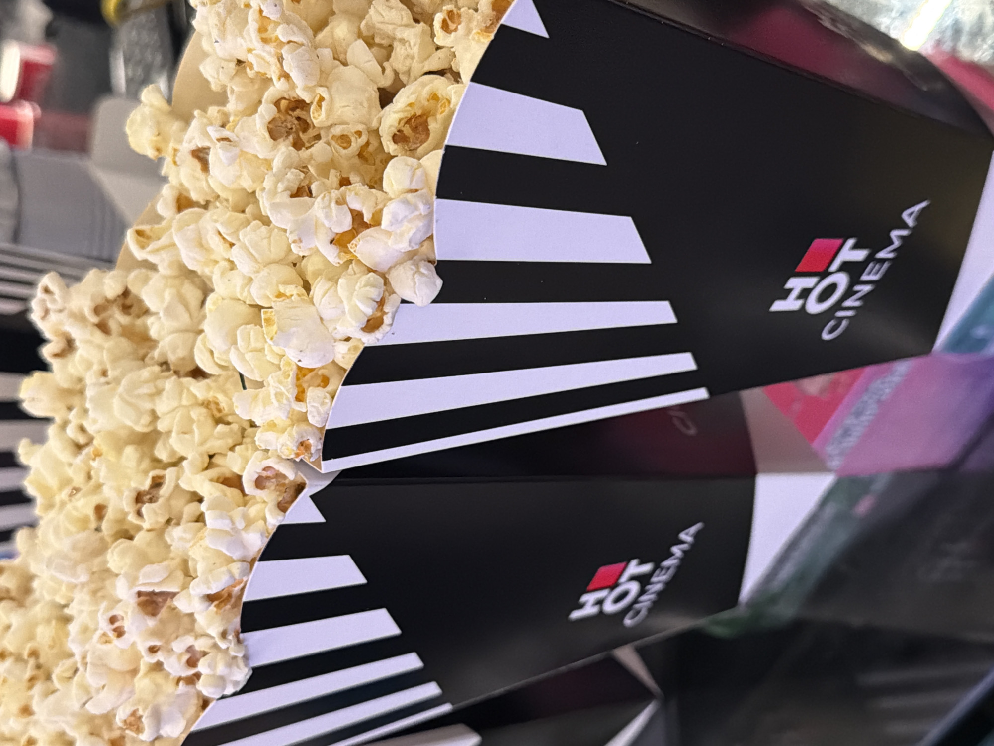 The image shows two black and white striped popcorn containers filled with popcorn. The containers have the words "HOT CINEMA" printed on them. The popcorn is overflowing from the containers. The scene appears to be indoors, possibly at a cinema in Rehovot, Israel, given the name "HOT CINEMA."