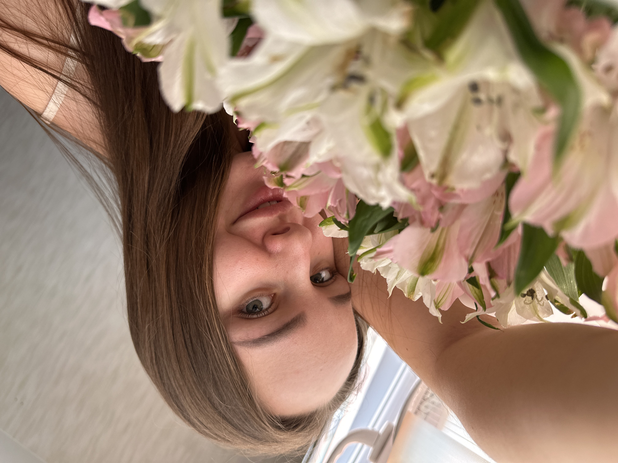 A woman with long brown hair is holding a bouquet of pink and white flowers. The picture is taken from an upward angle. The location of the image is unknown, and there is no way to determine if it was taken in Chaikovsky, Russia.