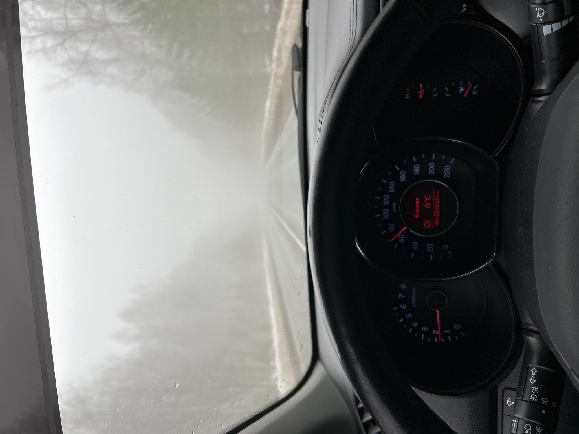 A driver's perspective from inside a car in Уральское, Russia, is presented. The foggy conditions obscure the view through the windshield, indicating low visibility. The dashboard is visible, displaying a temperature of 6°C. The car's odometer reads 224852 kilometers. The driver is traveling at approximately 2000 RPM.