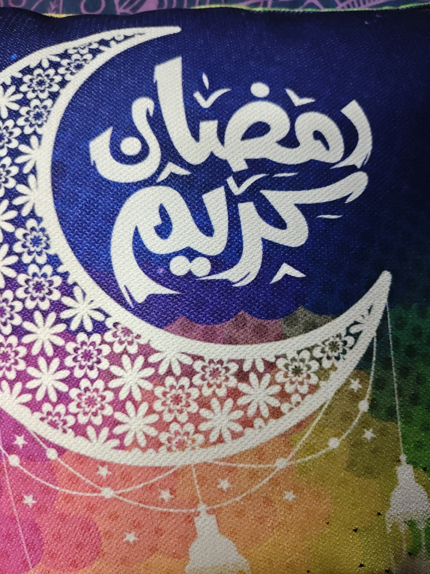 The image depicts a cushion or fabric with a design featuring a crescent moon shape filled with floral patterns. Within the crescent moon, there is Arabic calligraphy, presumably the phrase "Ramadan Kareem." Below the crescent moon, there are decorative elements resembling stars and lanterns. The background transitions through various colors, including blue, purple, pink, orange, yellow, and green. The image does not provide any information about the location in Боровково, Russia.
