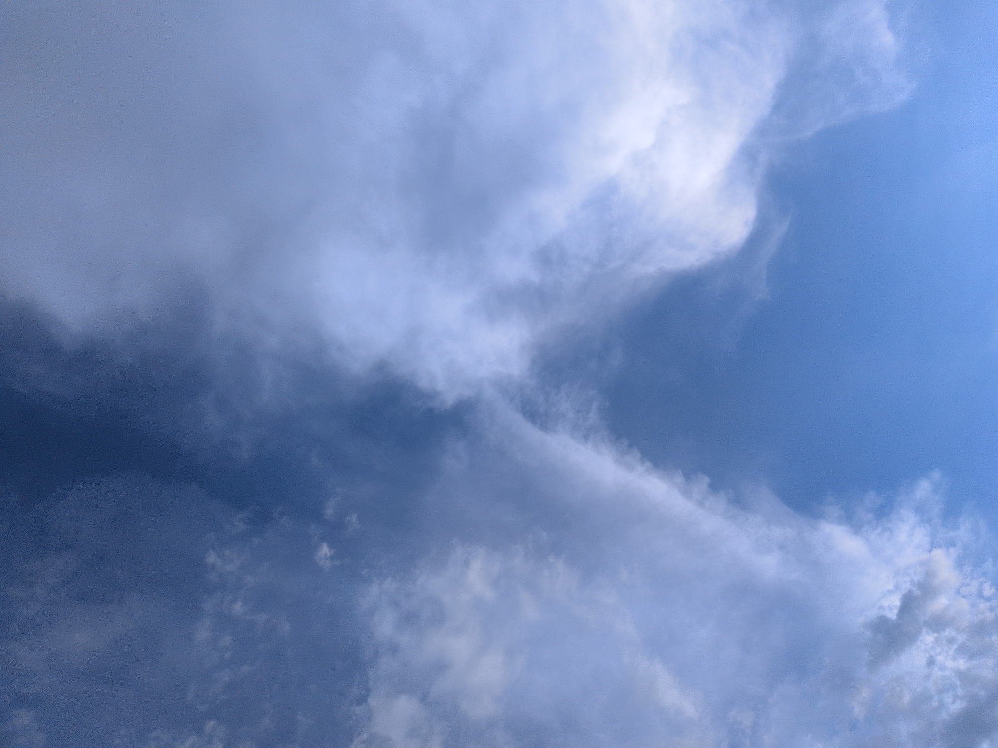 The image captures a section of the sky with a gradient of blue, transitioning from a deep blue at the top to a lighter, brighter blue towards the bottom. Wispy, translucent clouds are scattered across the sky, with some forming a V-shape that points downwards. The clouds are predominantly white and grey, with a soft, diffused texture. The overall impression is one of a slightly overcast but clear sky, with sunlight filtering through the clouds. The scene is devoid of any human presence or man-made structures, indicating a natural, outdoor environment. It is impossible to determine the exact location in Kapurkot, Nepal based solely on this image.