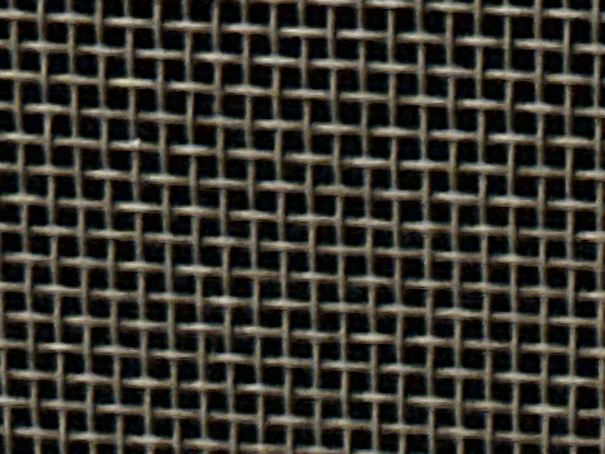 This is a close-up, abstract image of a wire mesh. The mesh is composed of thin, interlocking wires forming a grid pattern against a dark background. The wires appear to be metallic and have a slightly weathered or textured surface, reflecting light in subtle ways. There are no people, discernible objects, or specific environmental features visible, suggesting the image focuses solely on the texture and pattern of the mesh itself. The location in Dilijan, Armenia, is not visually represented in the image.