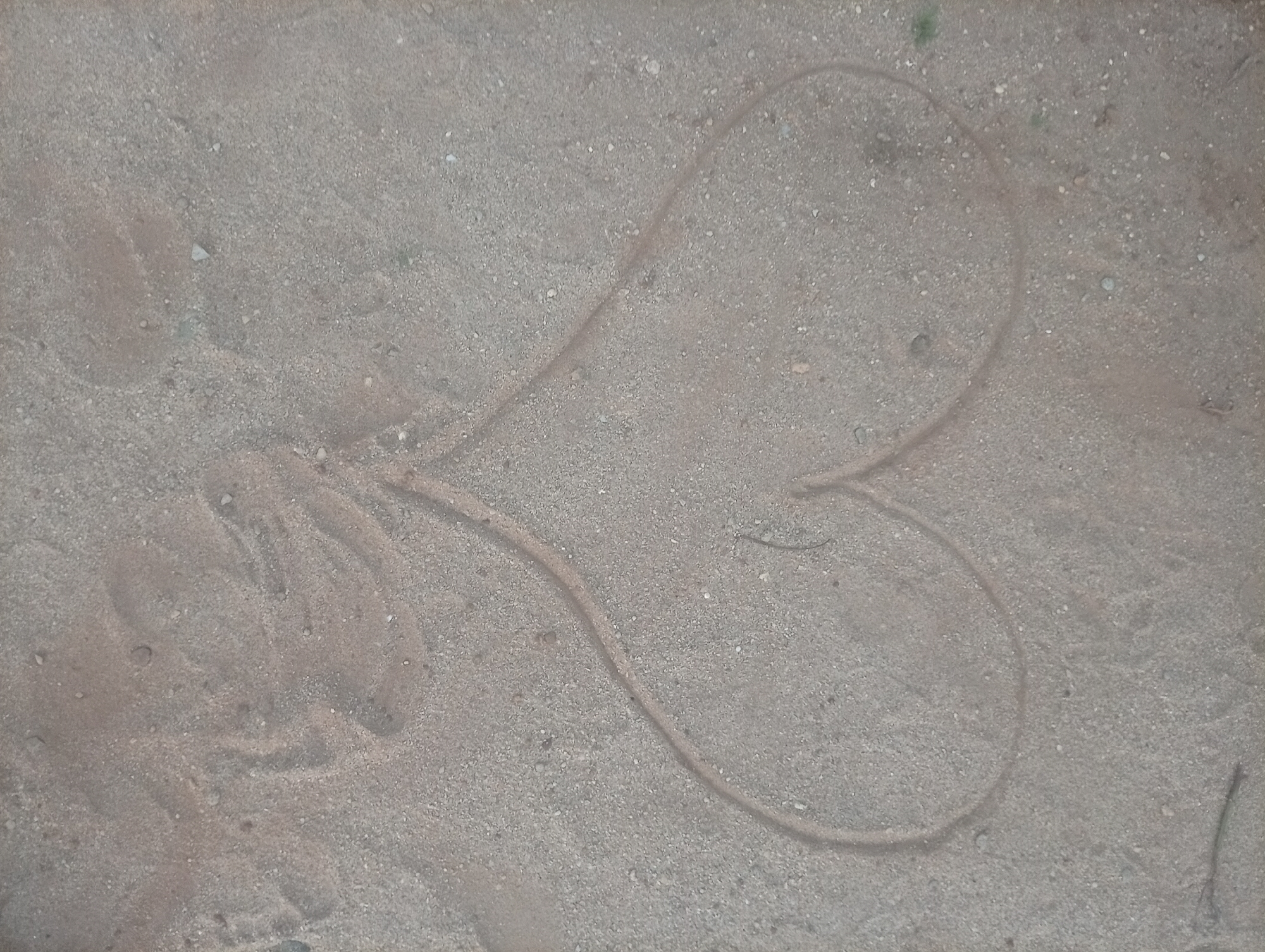 A heart shape is drawn in the sand. To the left of the heart shape there is a cluster of disturbed sand. The location is potentially Ikorodu, Nigeria. No people are visible.