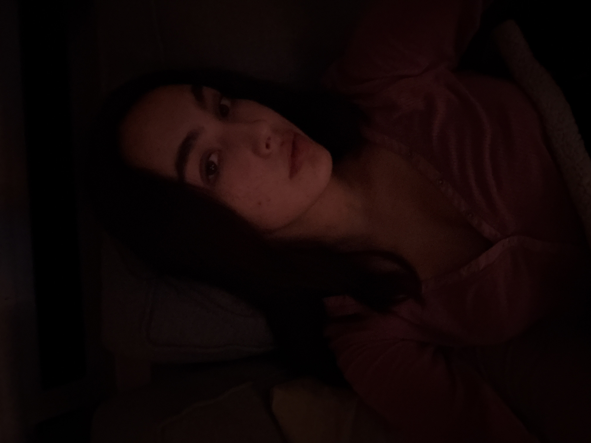 A young woman with long dark hair is lying on a couch or bed. She is wearing a pink top, and a light-colored blanket is partially visible near her. The scene is dimly lit. The location is unknown, and there are no visible landmarks that would indicate it is in Mexico City, Mexico.