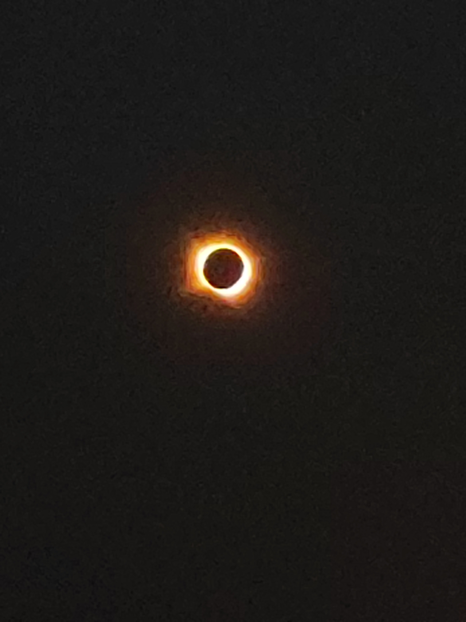 The image displays a celestial event, likely a solar eclipse, captured against a dark, possibly night sky. A distinct, luminous ring of light, an annulus, encircles a dark central disc. The color of the ring is predominantly orange and yellow, suggesting the sun's corona. The backdrop is a deep black, indicating a lack of ambient light or a vast expanse of space. There are no discernible human subjects, objects, or architectural elements from the city of Autillo de Campos, Spain, in the image. The composition is focused entirely on the astronomical phenomenon.