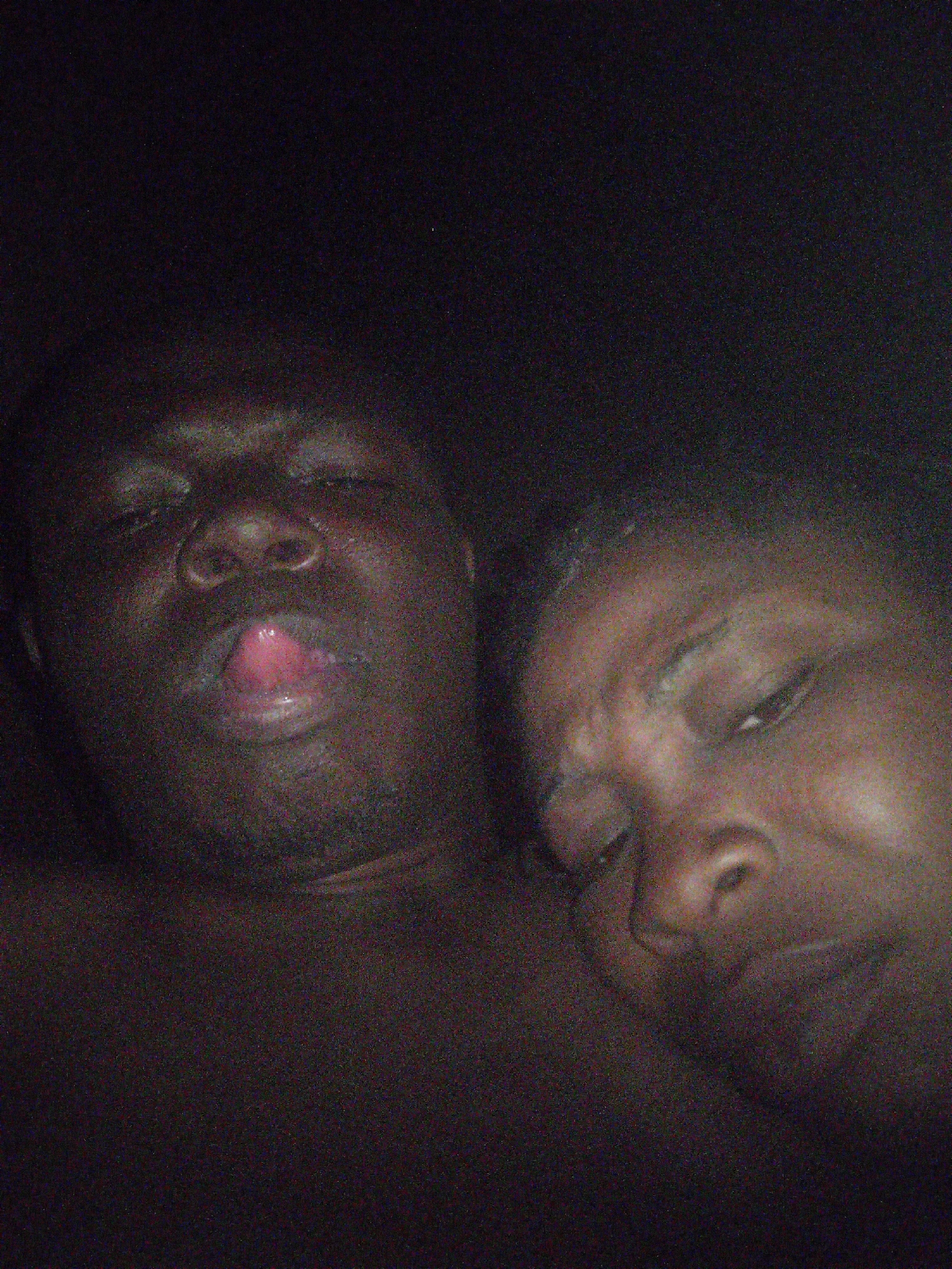 Two dark-skinned individuals are in close proximity. The individual on the left is a male with his mouth slightly open and tongue protruding. The individual on the right is a female with her eyes closed. The background is dark and indistinct. The city of Unknown, Unknown is not mentioned.