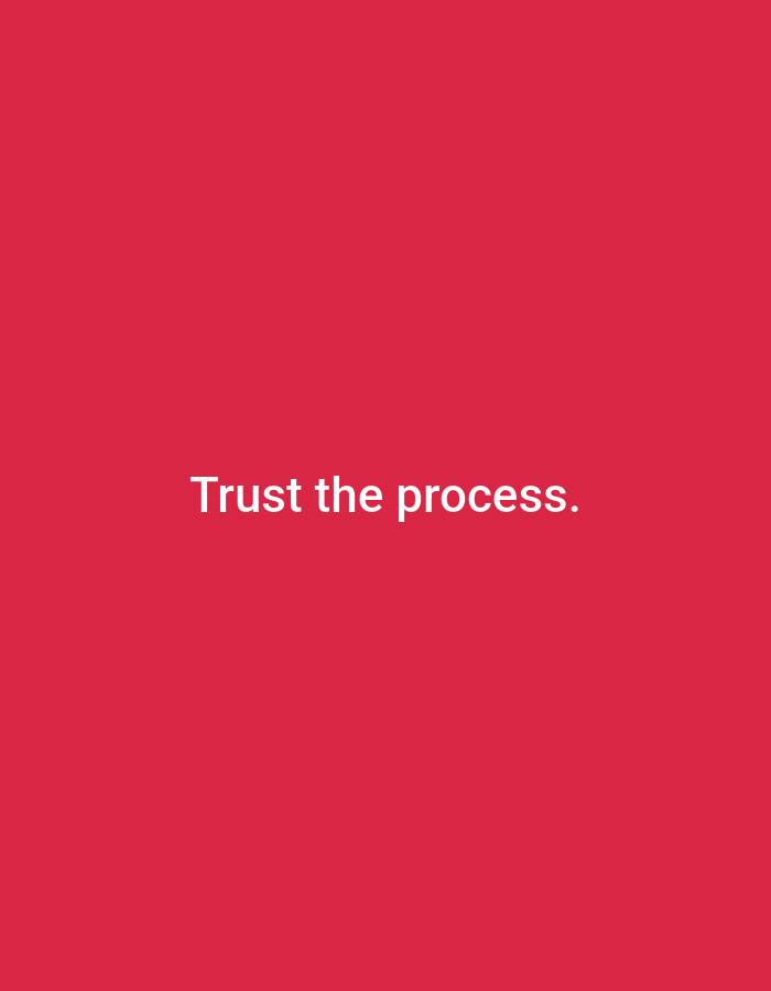 A minimalist, high-angle shot features a plain red background. White text in the center of the frame reads "Trust the process." The image lacks any specific geographical markers or human presence, and therefore cannot be associated with Ramraj, India, or any particular urban environment.