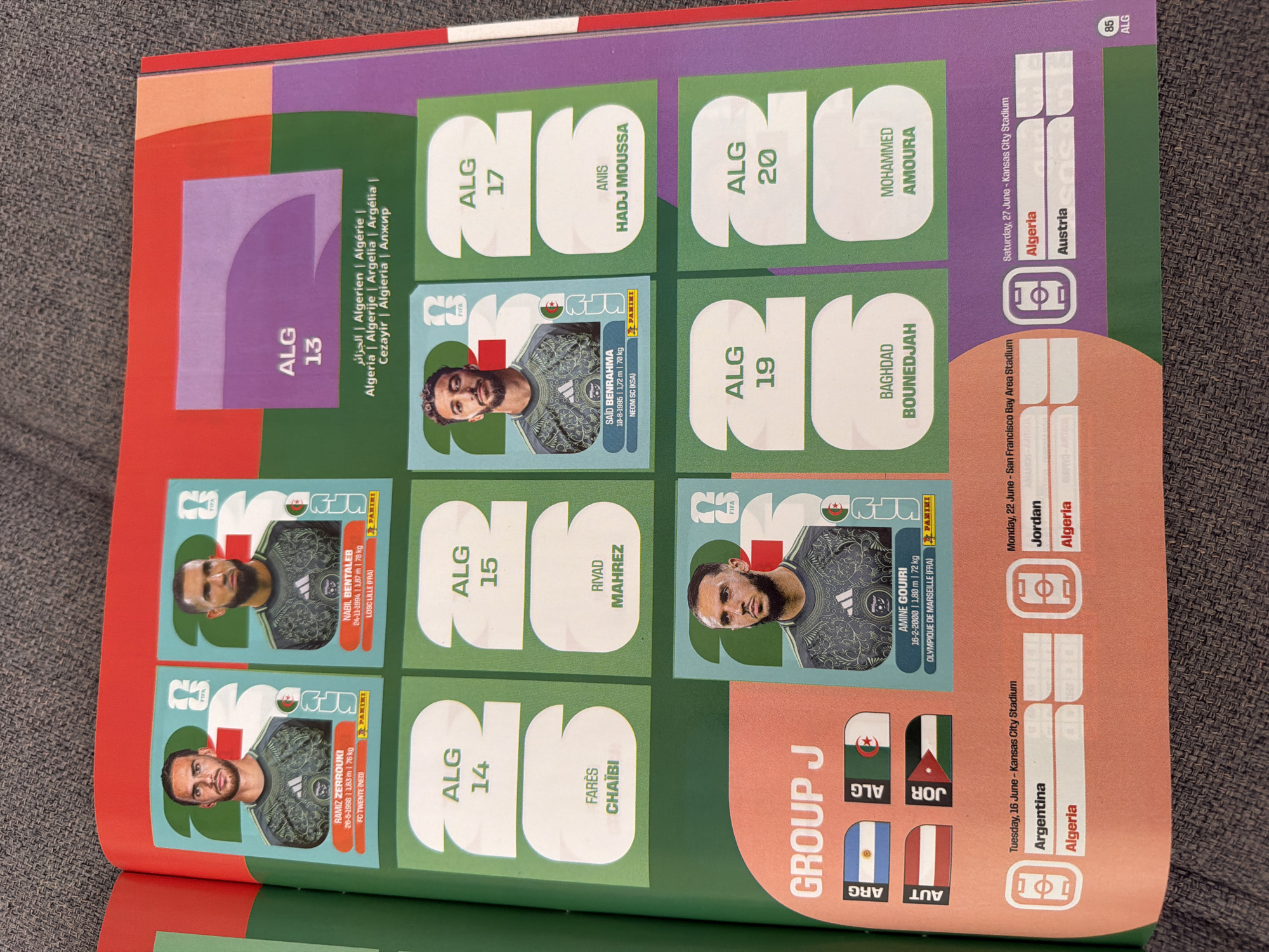 The image is a page from a sticker album, likely related to the FIFA World Cup, featuring players from Algeria. The album page displays player stickers, their names, and country codes. There are several player stickers with their respective images and biographical information, such as name, birthdate, height, weight, and club. Some stickers have the FIFA logo and the Panini logo. The page also includes a section labeled "GROUP J" with country flags representing Argentina, Algeria, Australia, and Jordan. Additionally, there are scheduled match dates and locations, with "Kansas City Stadium" and "San Francisco Bay Area Stadium" mentioned. The page exhibits a color palette of green, red, orange, and purple. The surrounding environment appears to be a textured fabric surface, possibly a carpet or textile. The image is sharp and well-lit, capturing the details of the stickers and the album page. There is no information about Zlatitrap, Bulgaria, in the provided image.